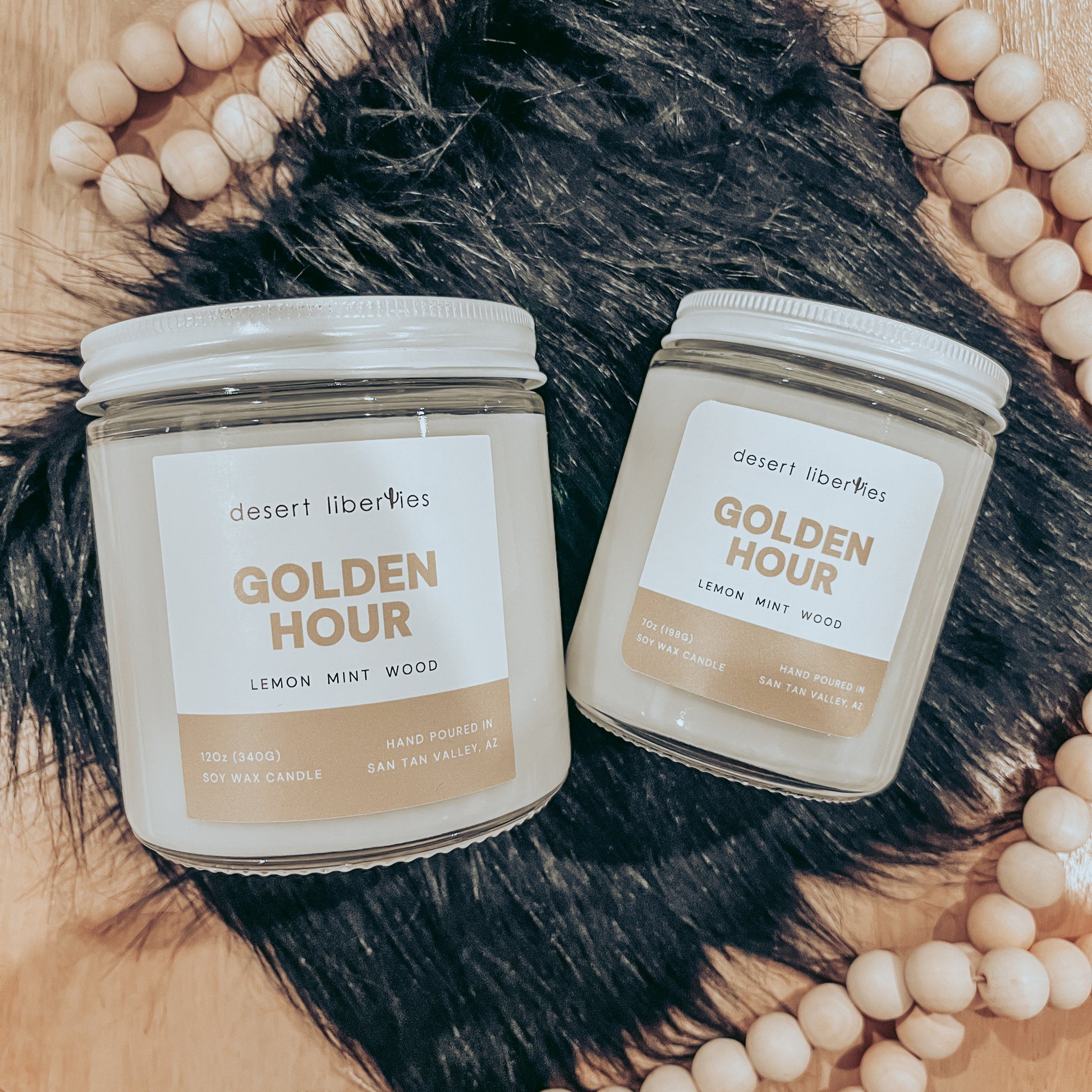 Two candles with white labels, one small and one medium, in clear glass jars. The labels say 'GOLDEN HOUR' and list fragrance notes.