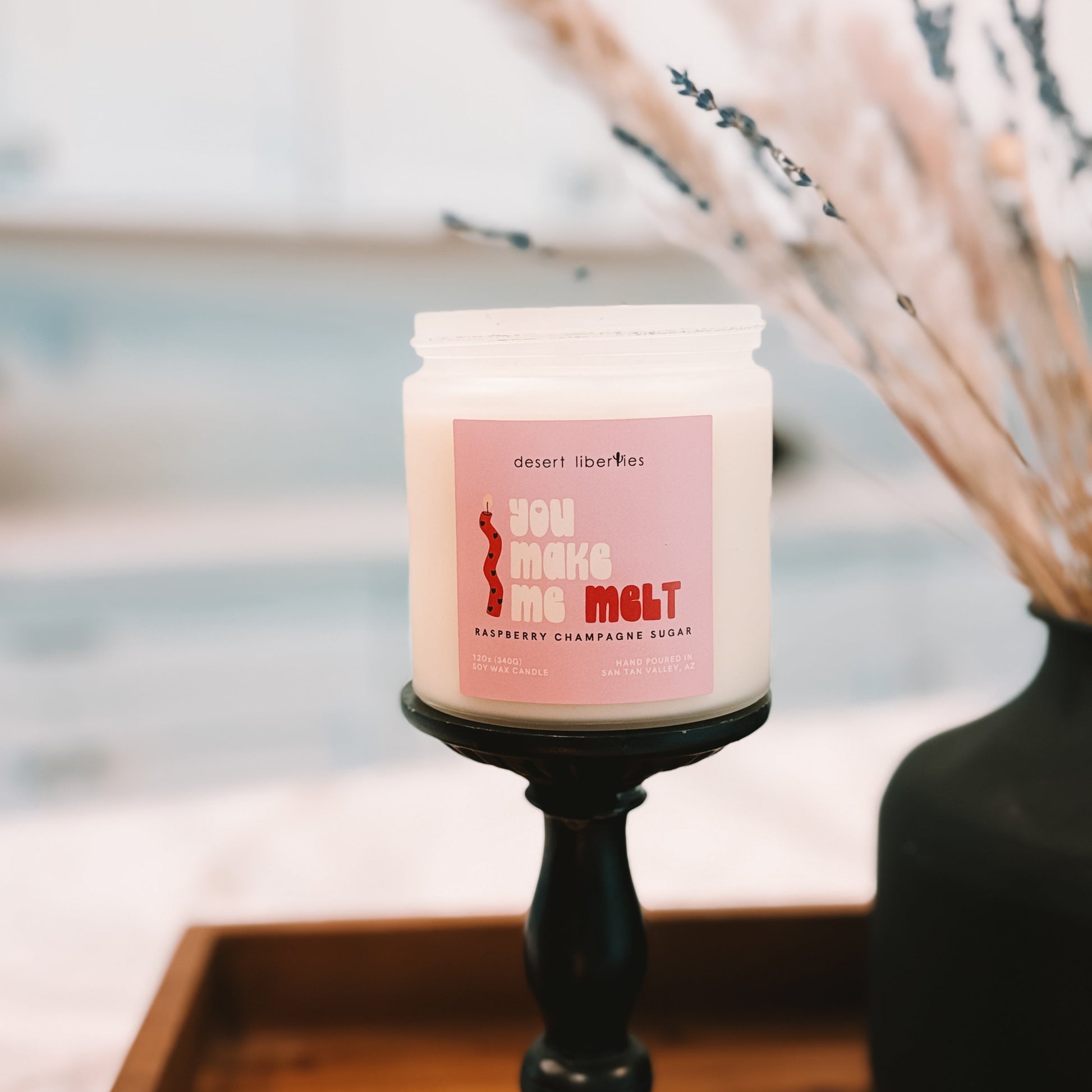 Candle with a pink label on a black candlestick holder against a blurred background