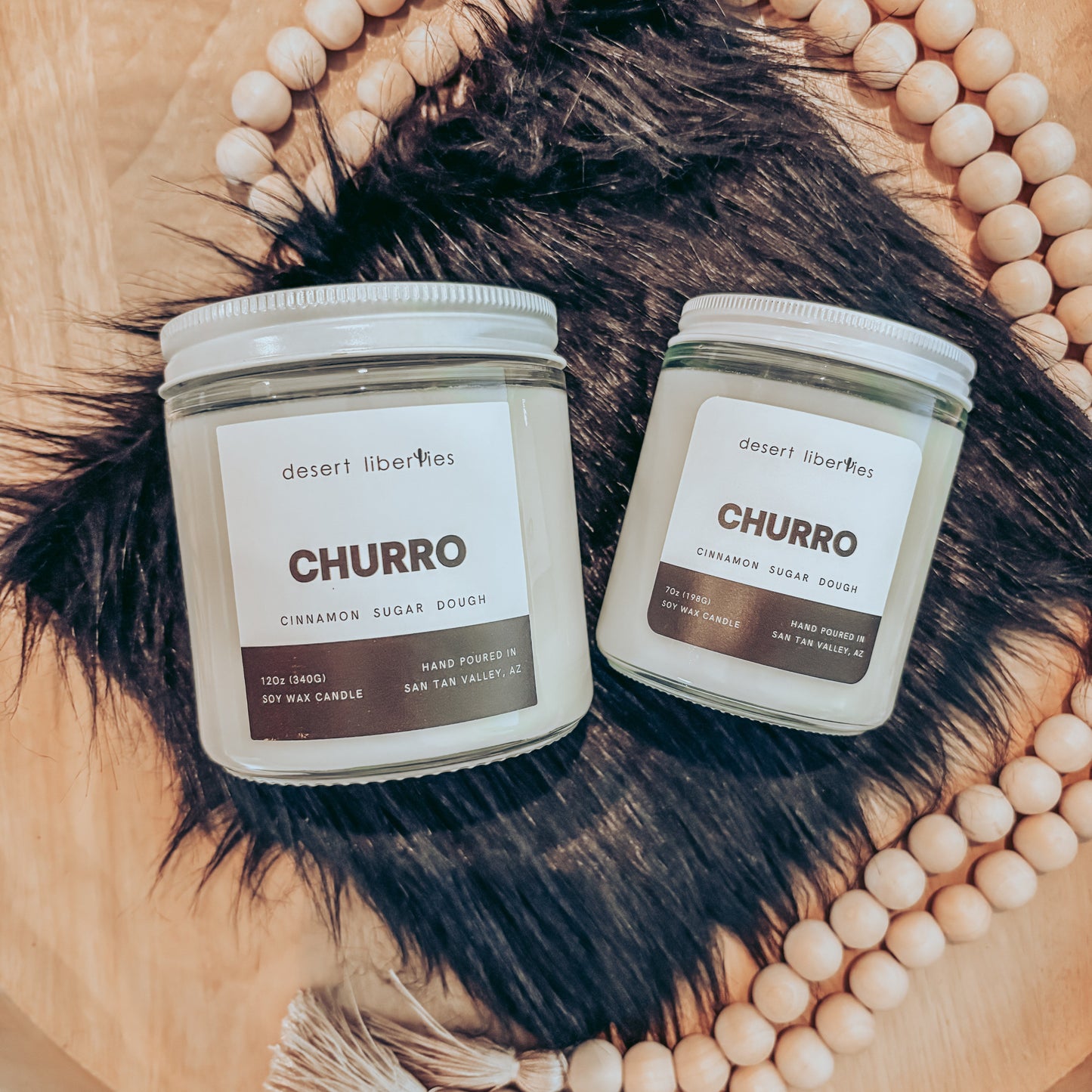 Two "Churro" candles on a black fur and wood surface.