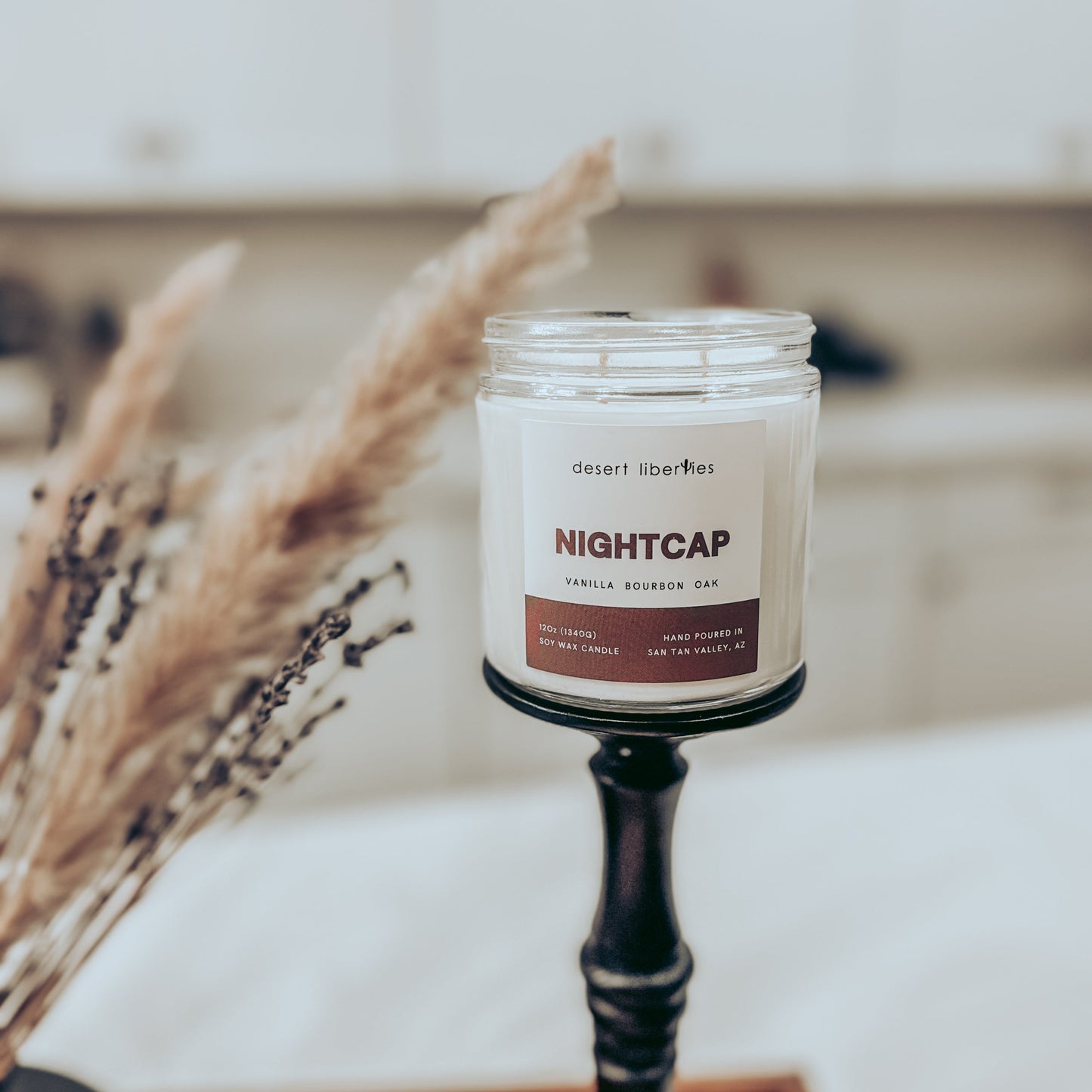 Candle labeled 'Nightcap' on a stand with dried plants in the background