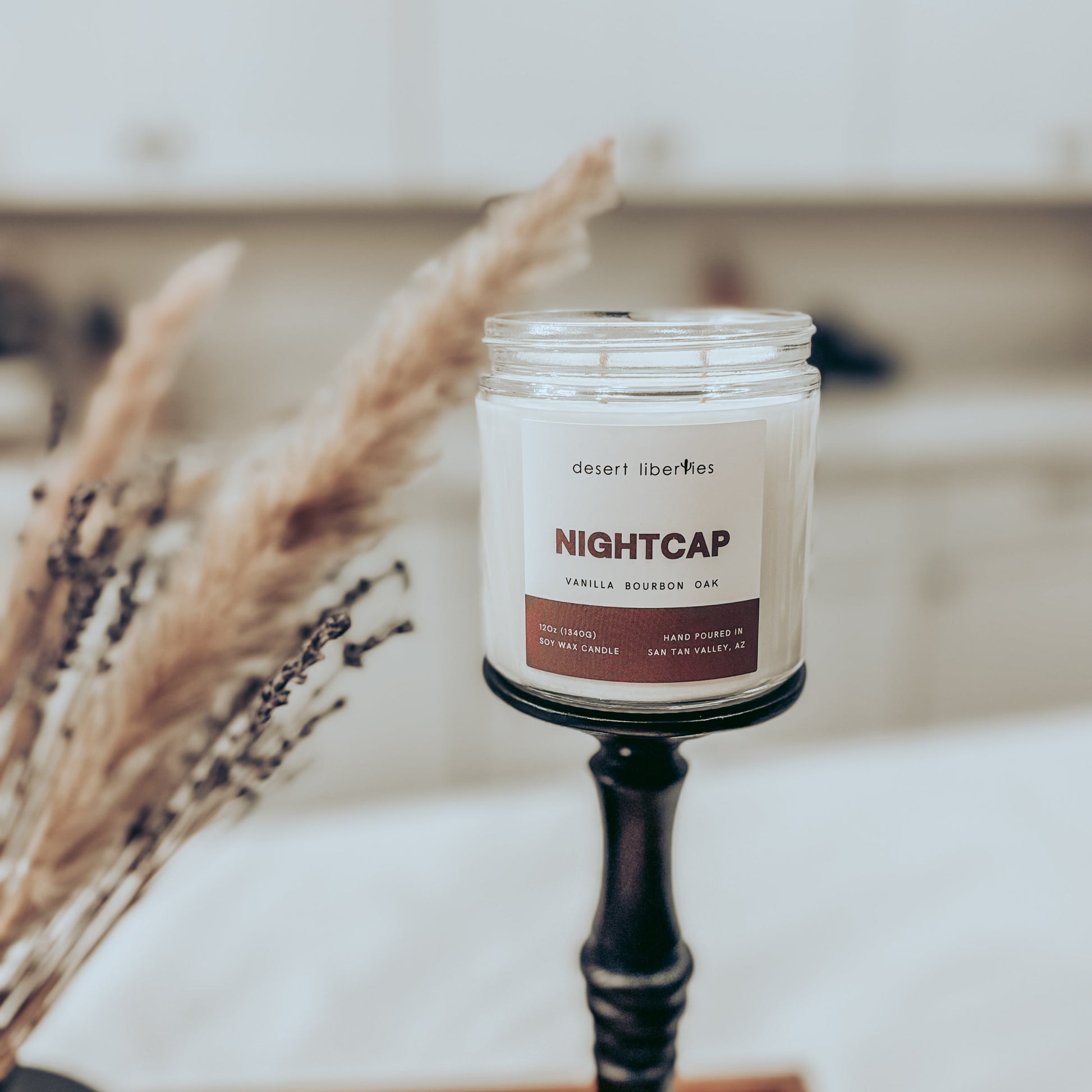 Candle labeled 'Nightcap' on a stand with dried plants in the background