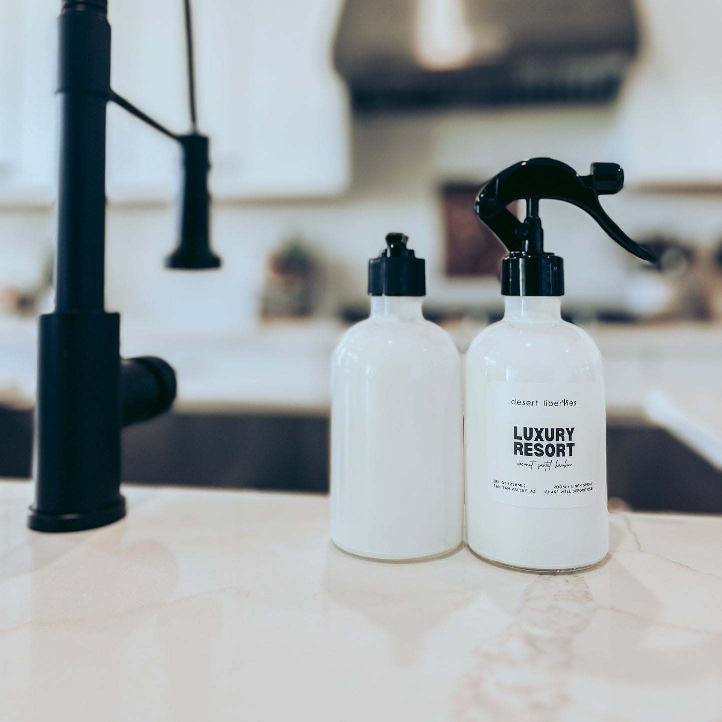 Two bottles labeled 'Luxury Resort' on a kitchen counter with a black faucet in the background.