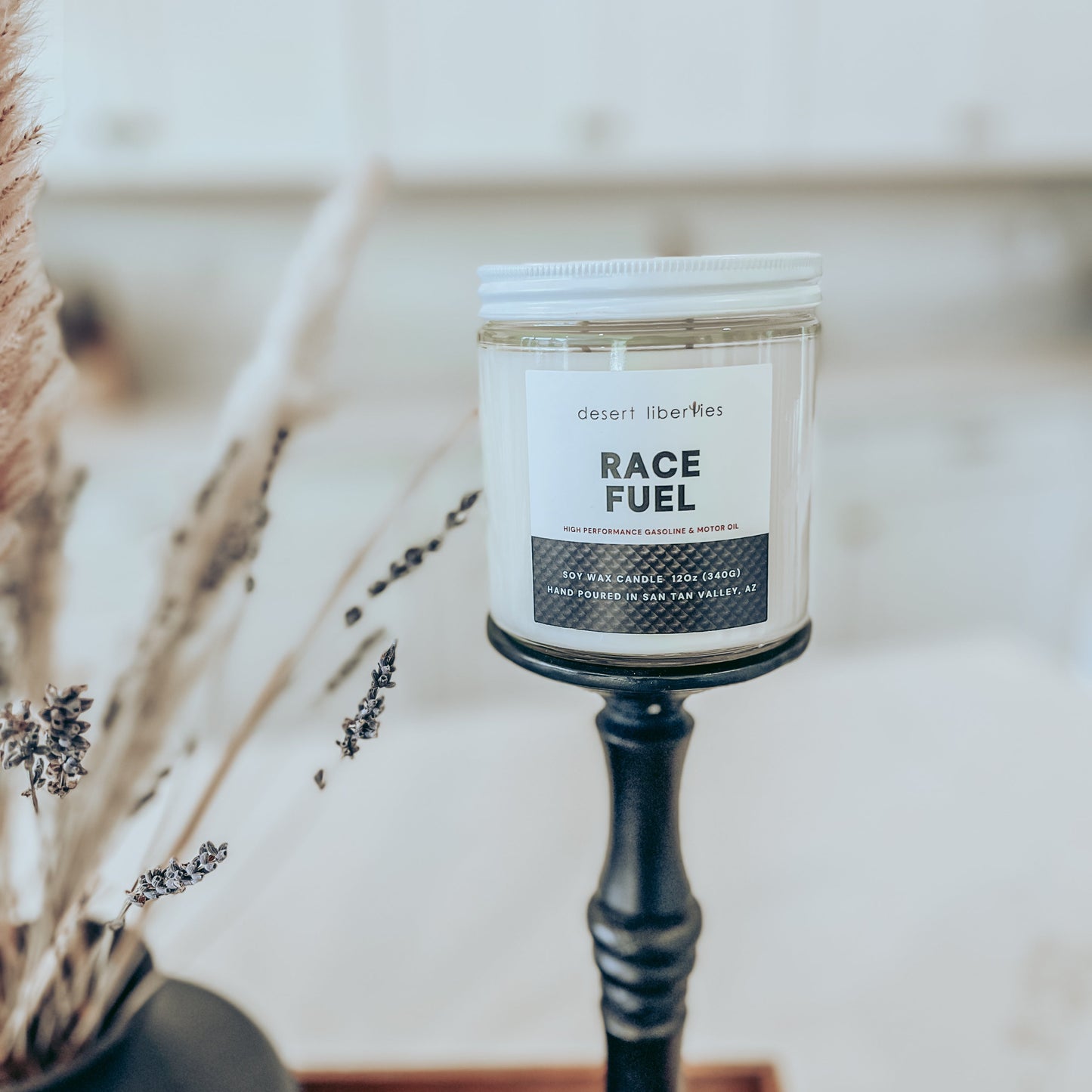 Race fuel scented candle on a black candlestick and blurred kitchen background.