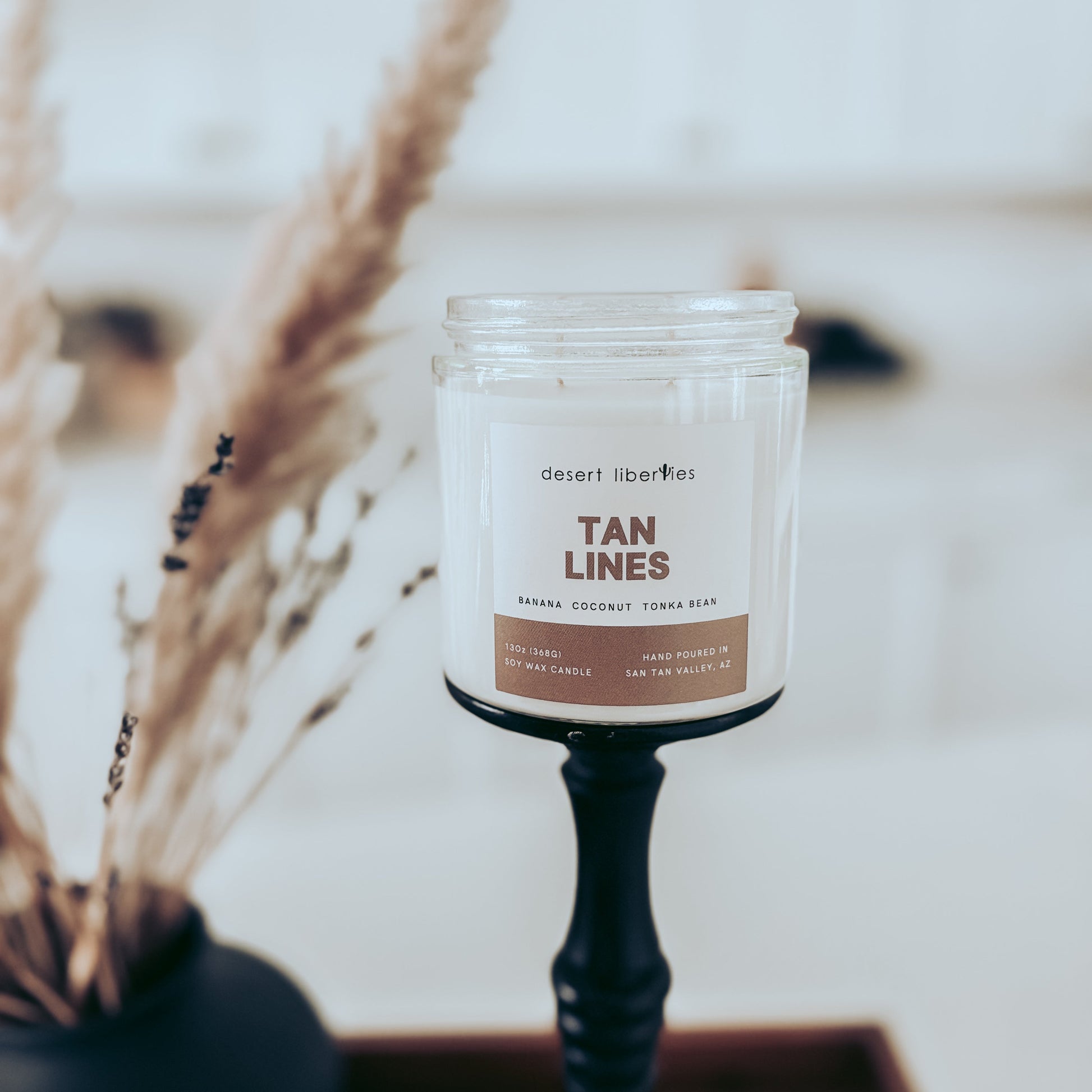Candle labeled 'Tan Lines' with decorative elements in the background