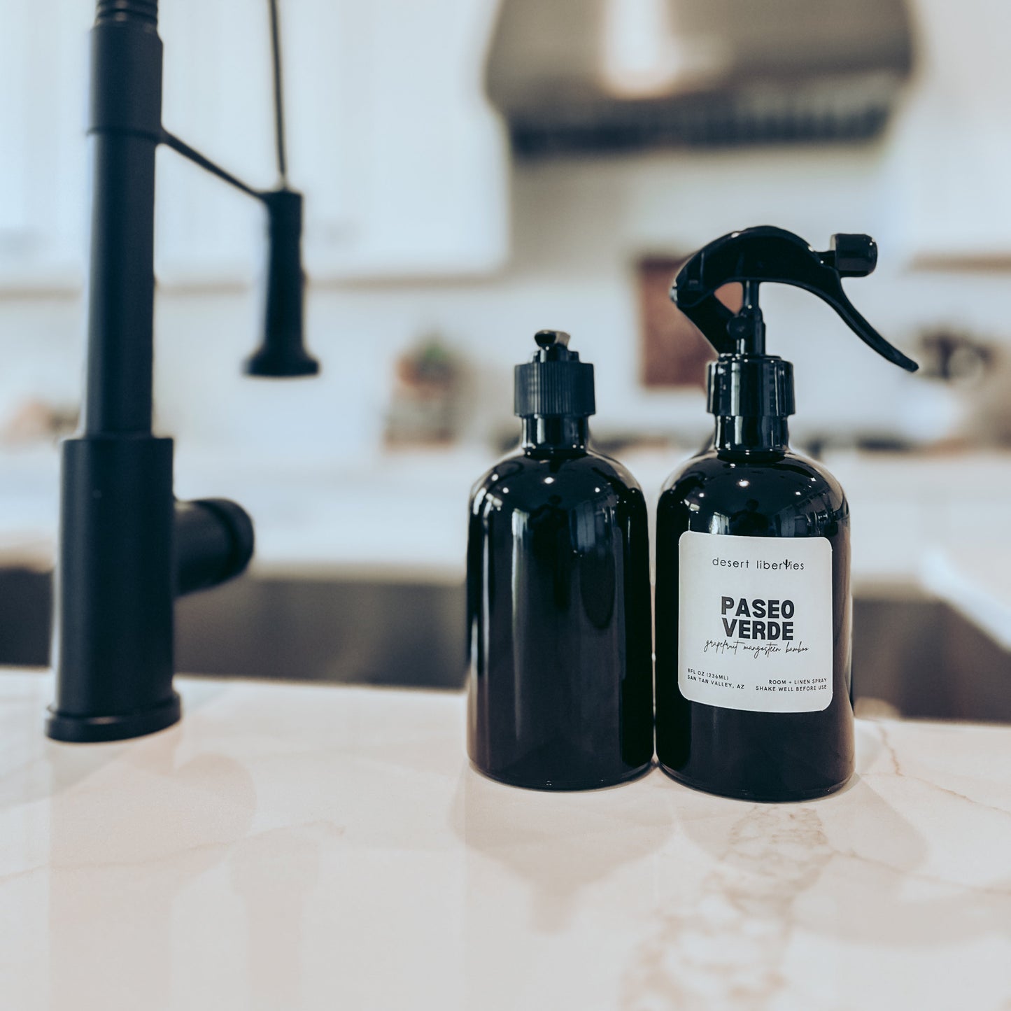 Two black bottles with labels on a kitchen counter with a faucet in the background.