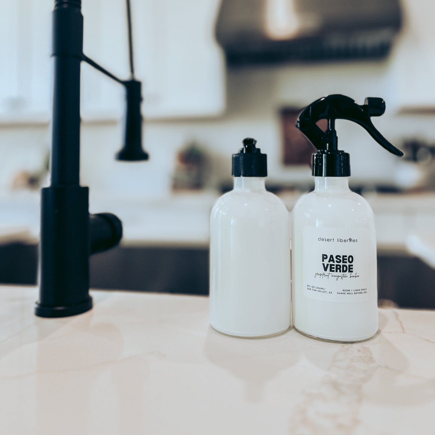 Two white bottles with black sprayers on a kitchen counter.