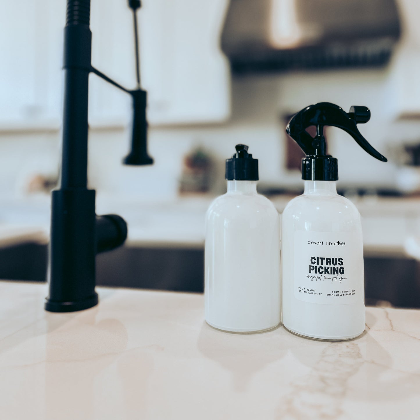 Two white bottles with black sprayers on a kitchen counter with a black faucet in the background.