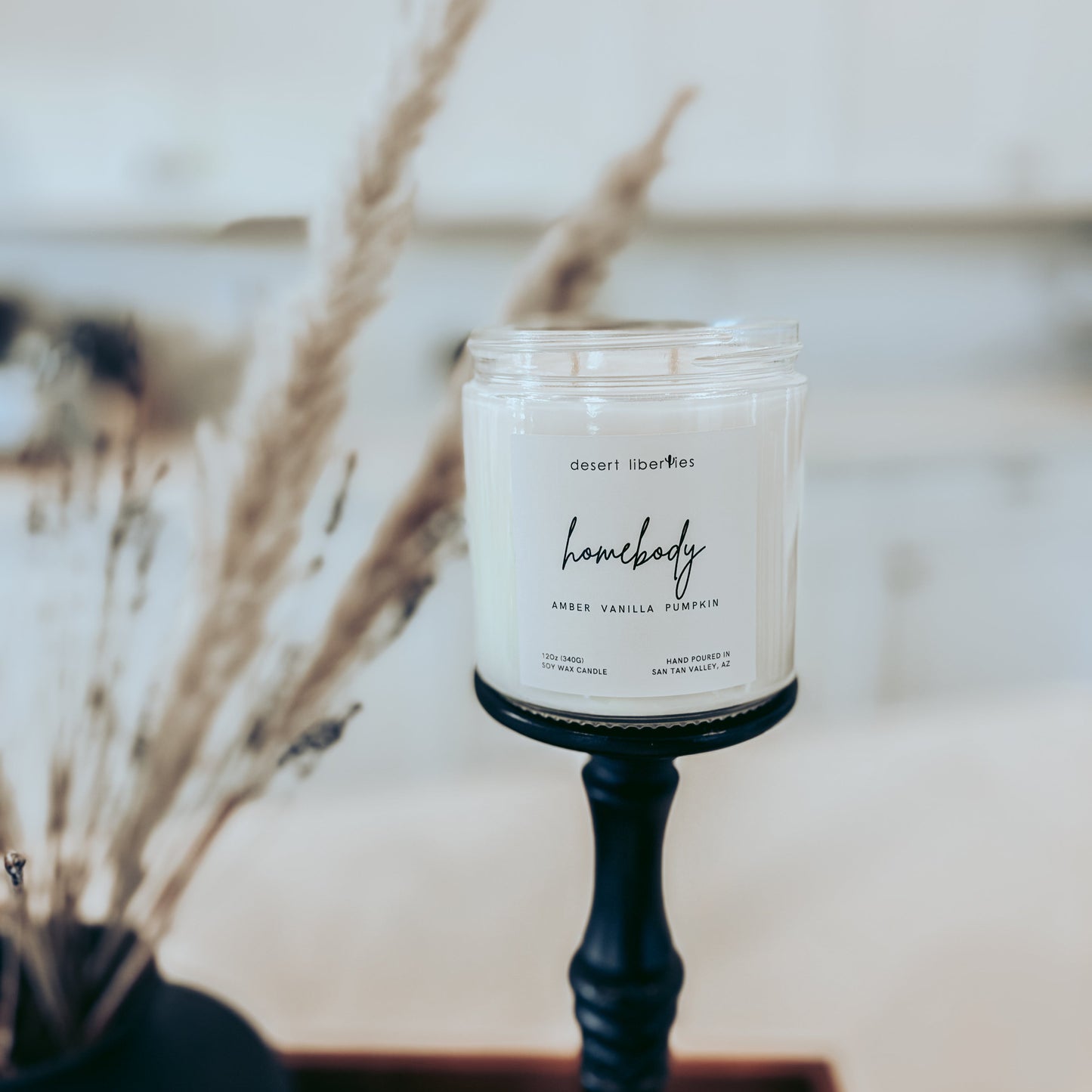 Candle labeled 'homebody' on a stand with dried plants in the background