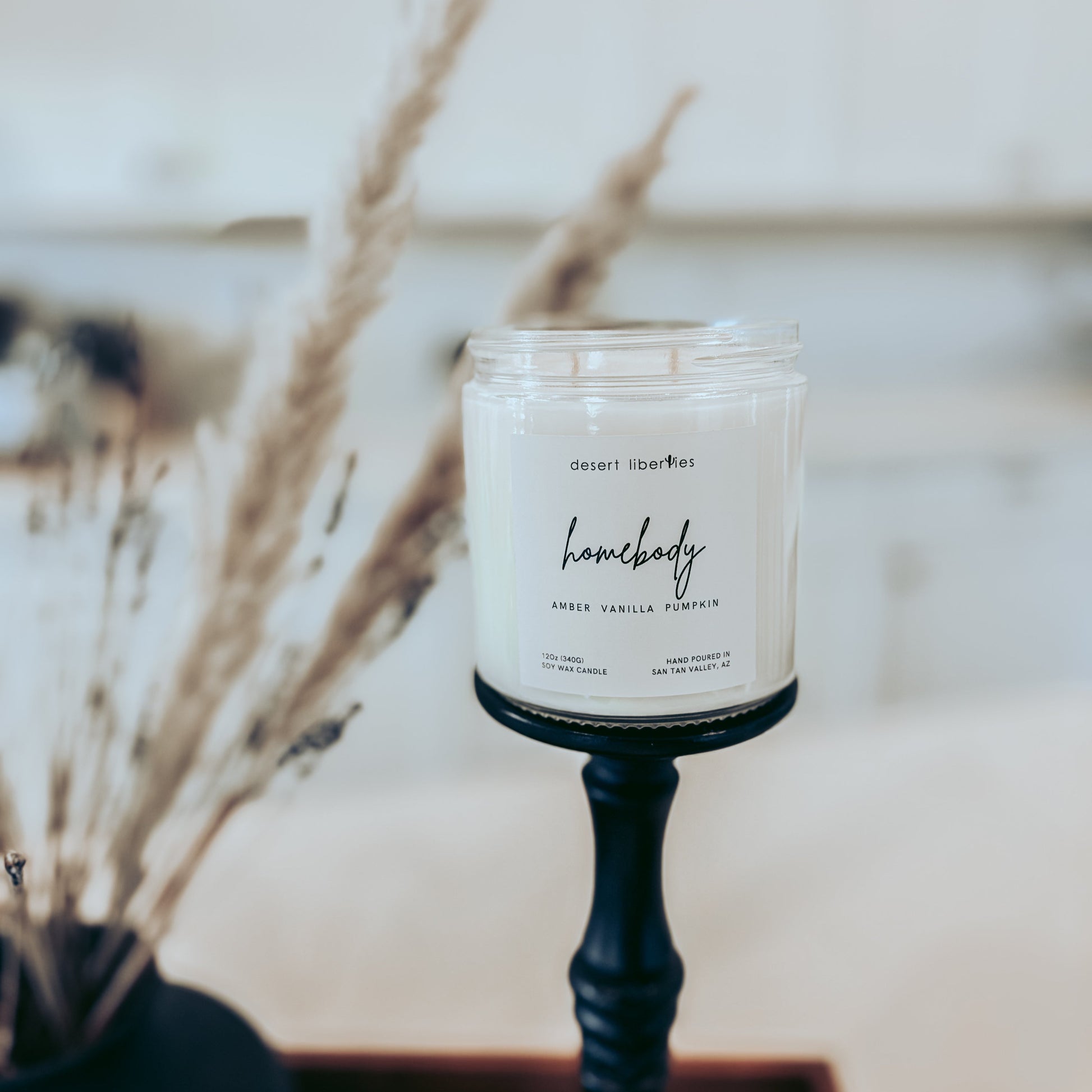 Candle labeled 'homebody' on a stand with dried plants in the background