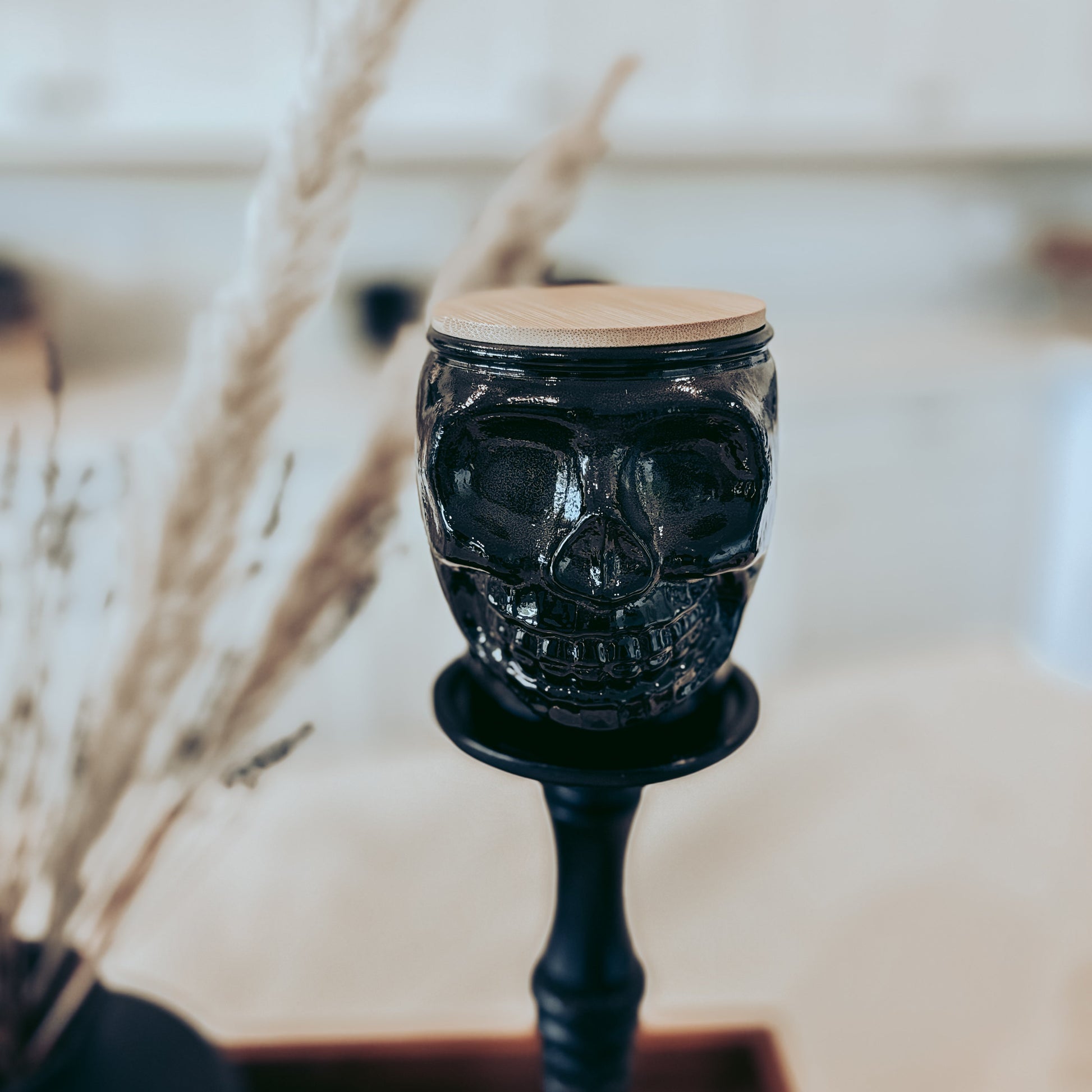 Black skull-shaped candle holder on a stand with a blurred background