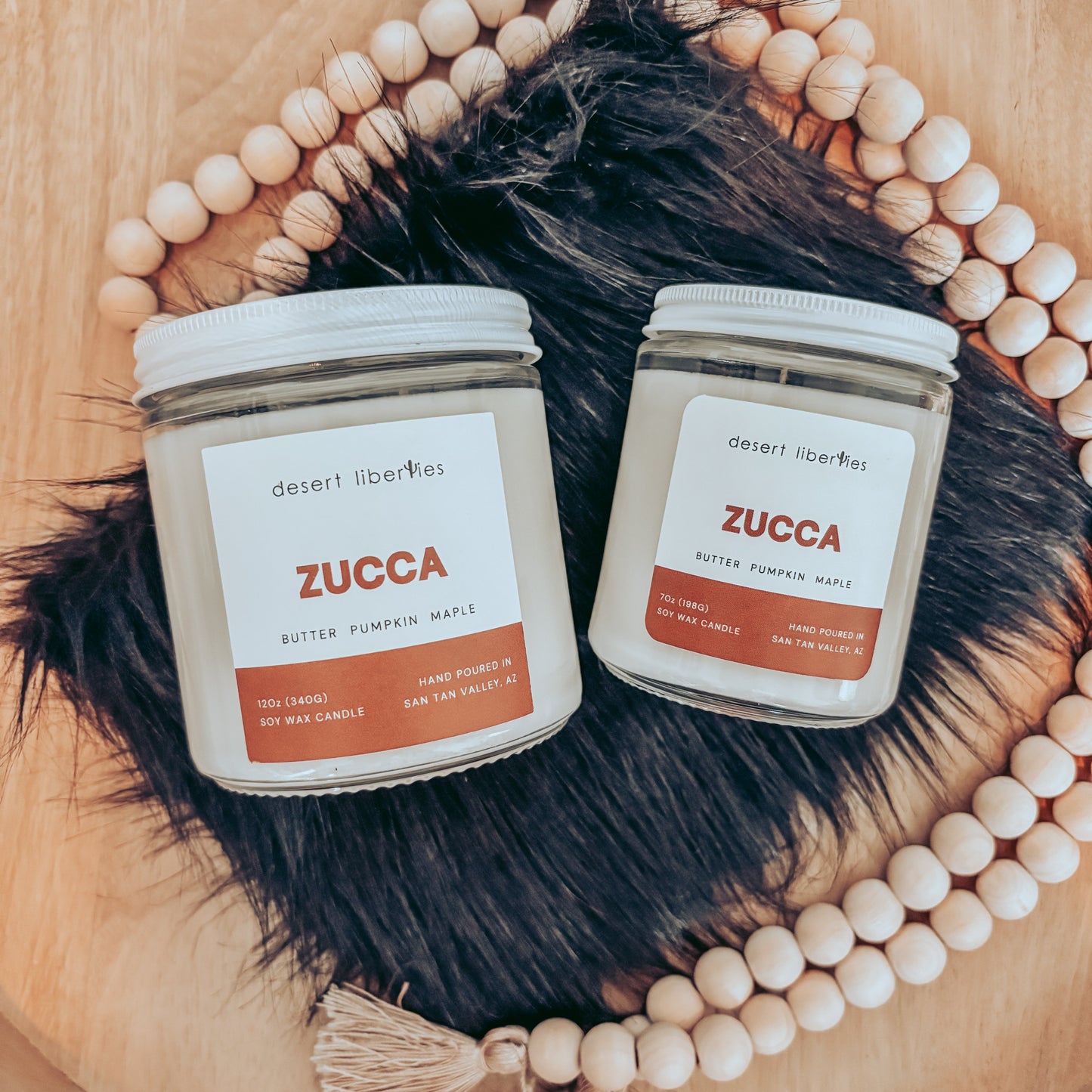 Two Zucca candles on a wooden surface with decorative elements