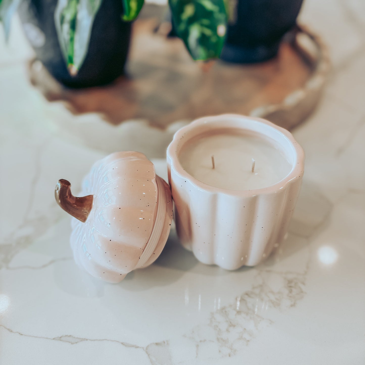 Blush pink pumpkin canister candle, with top off, on a white marble surface. 