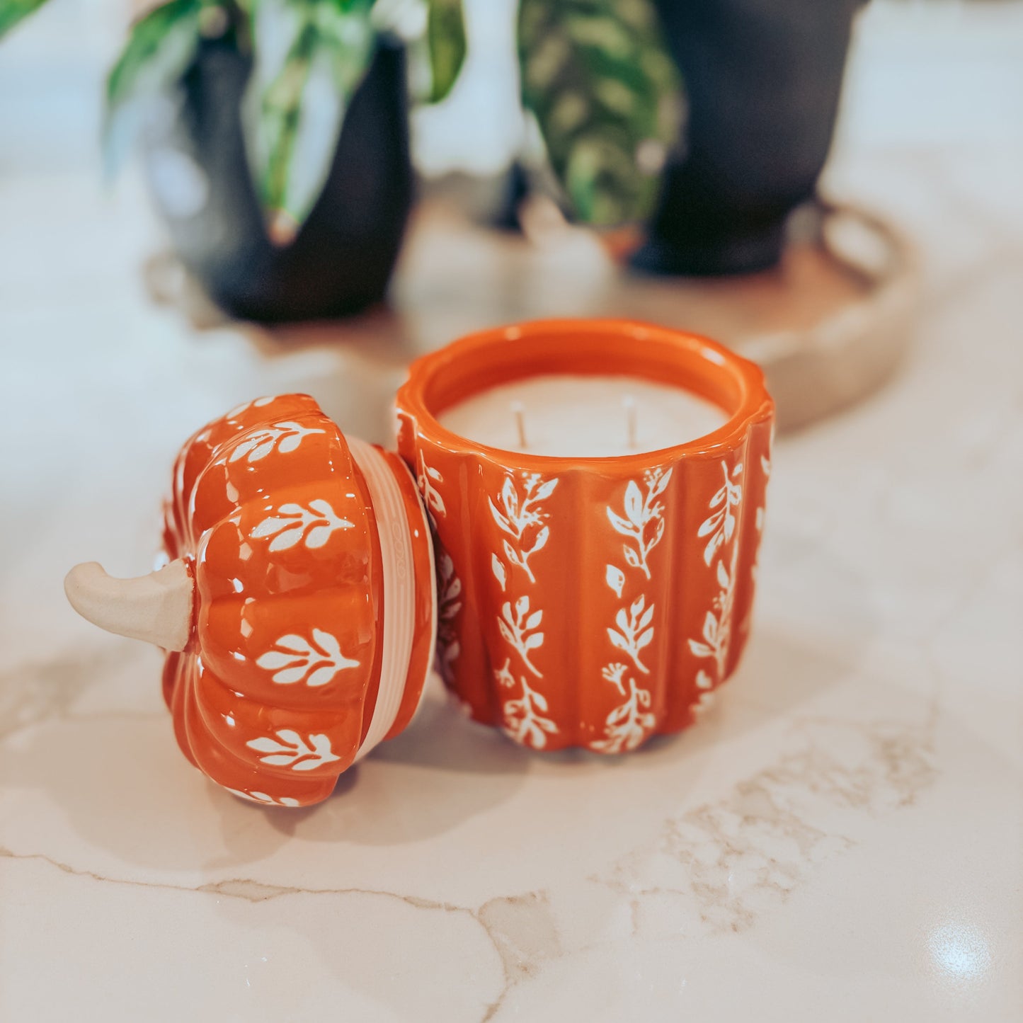 Orange candle with floral design on a marble surface with plants in the background