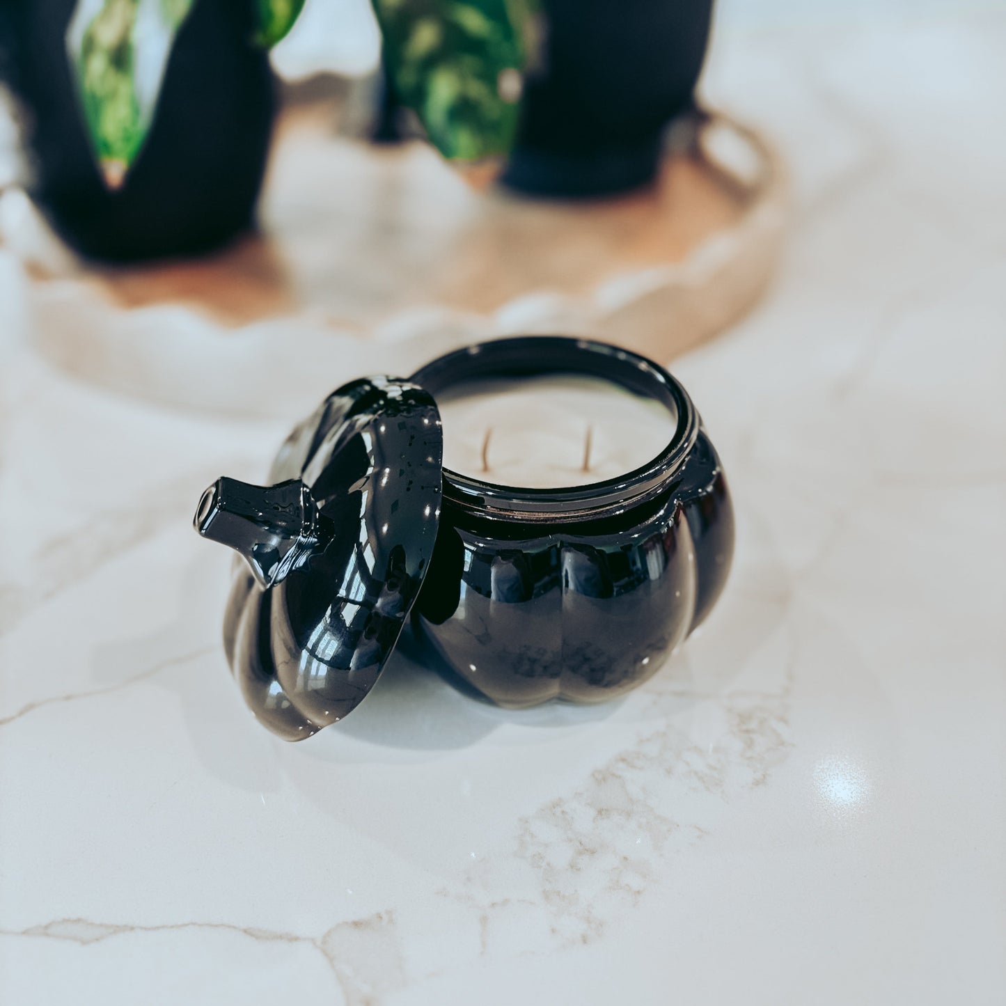 Black glass pumpkin jar with a candle on a marble surface, with a plant in the background.