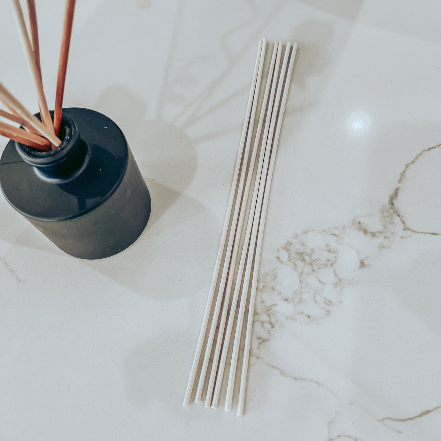 6 reeds on a marble surface with a matte black reed diffuser off to the side.