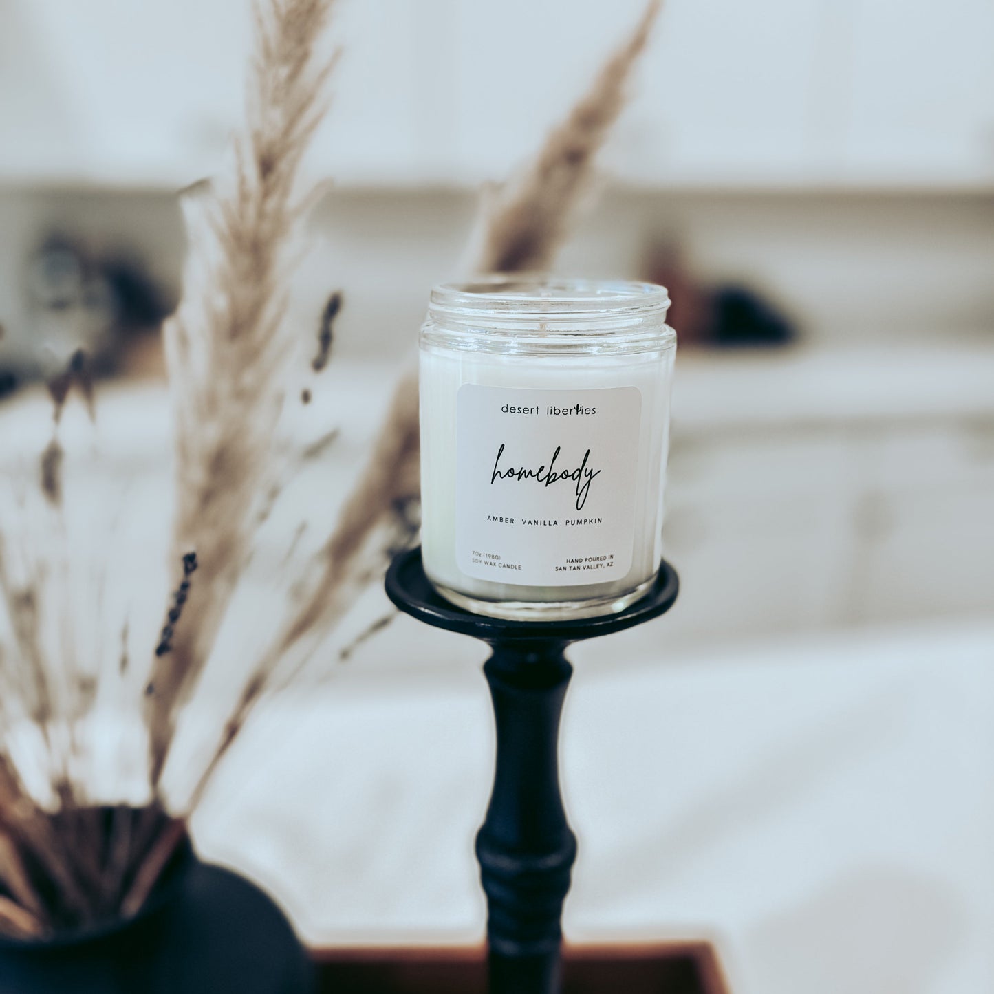 Candle in a jar on a black stand with dried plants in the background