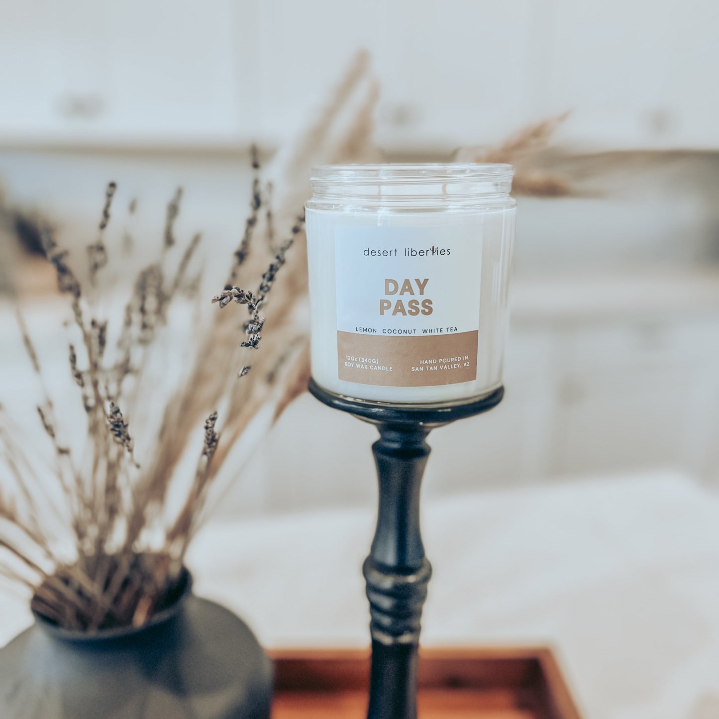 One candle on a black candlestick with dried plants in the background and a blurred kitchen background. 