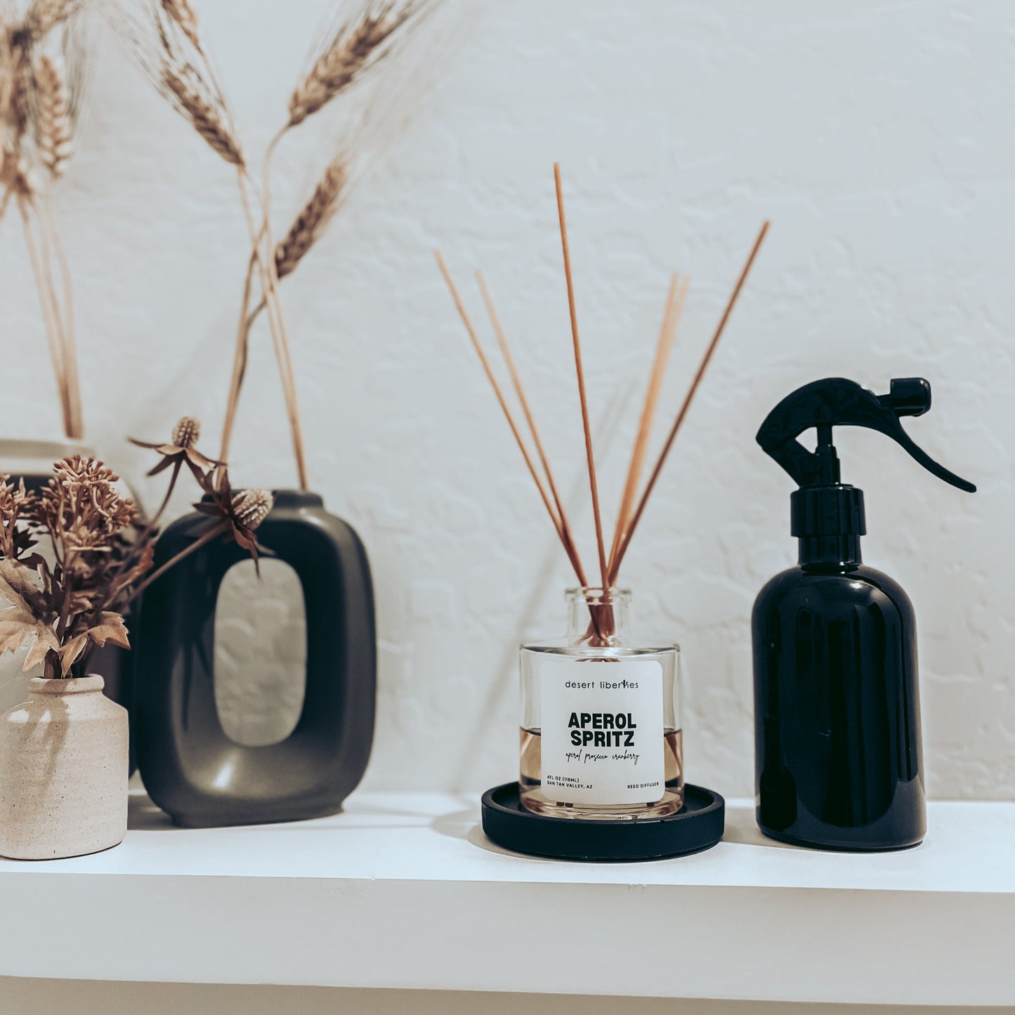 Decorative items including a black spray bottle, glass bottle with reeds, and ceramic vase on a shelf.