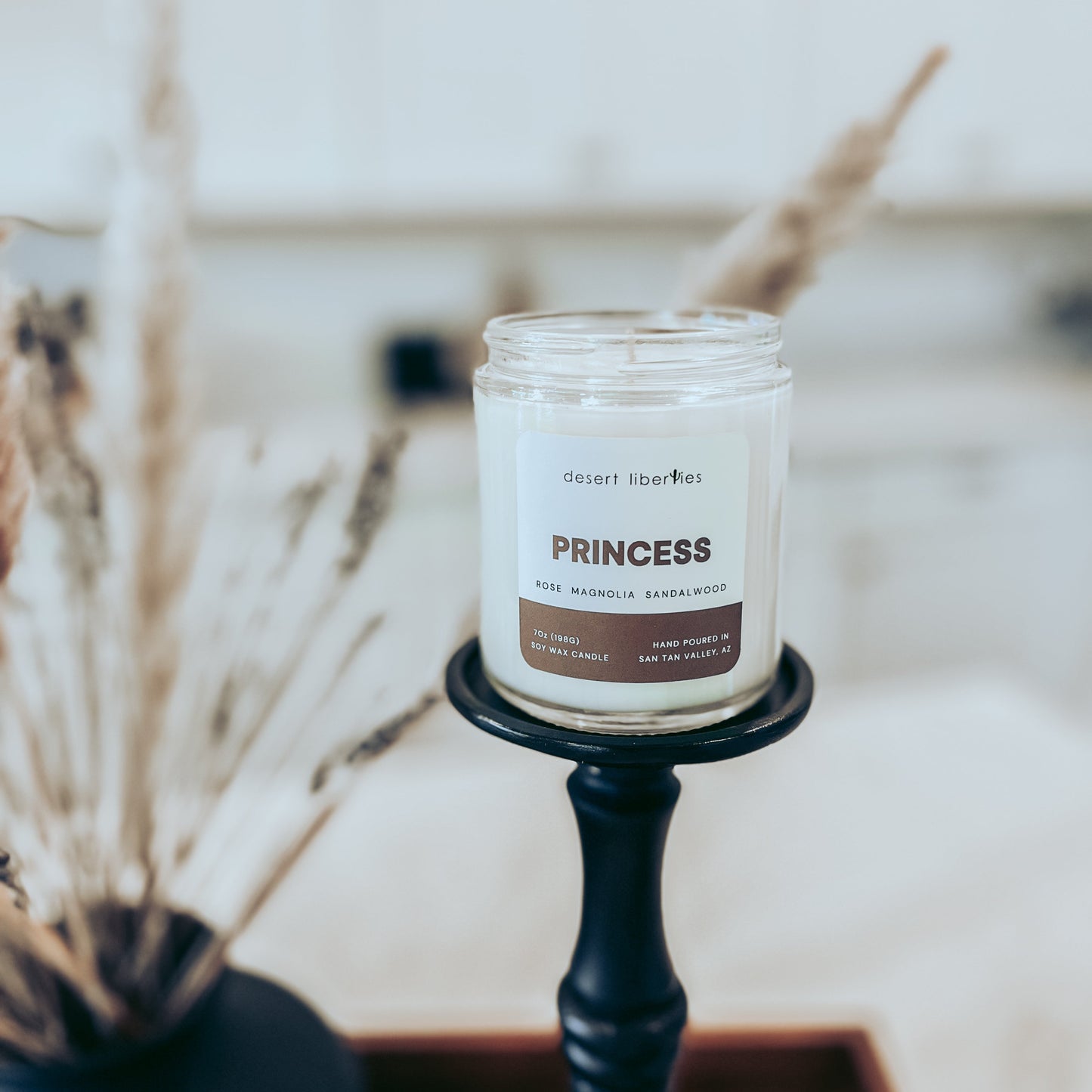 Candle labeled 'Princess' on a black holder with dried plants in the background