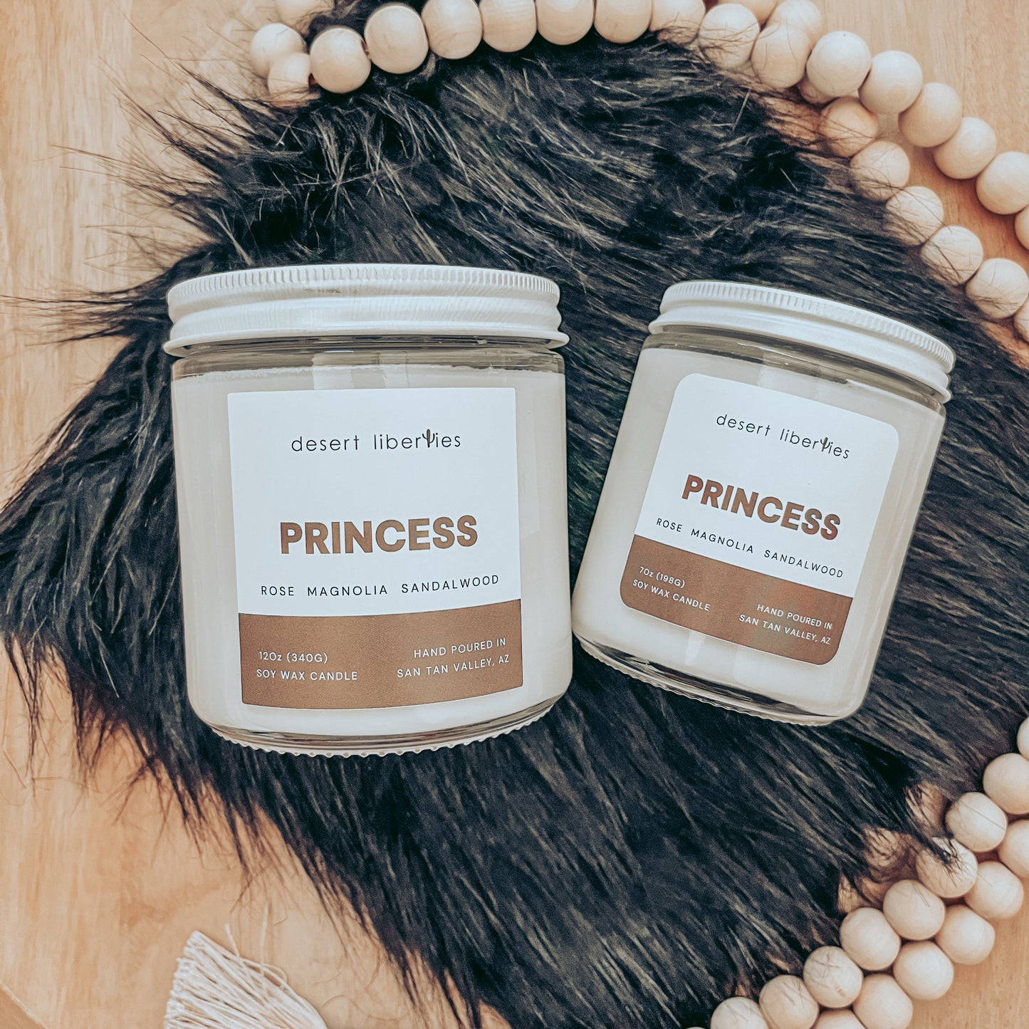 Two 'Princess' candles by Desert Liberties on a fur surface with beads and tassels.