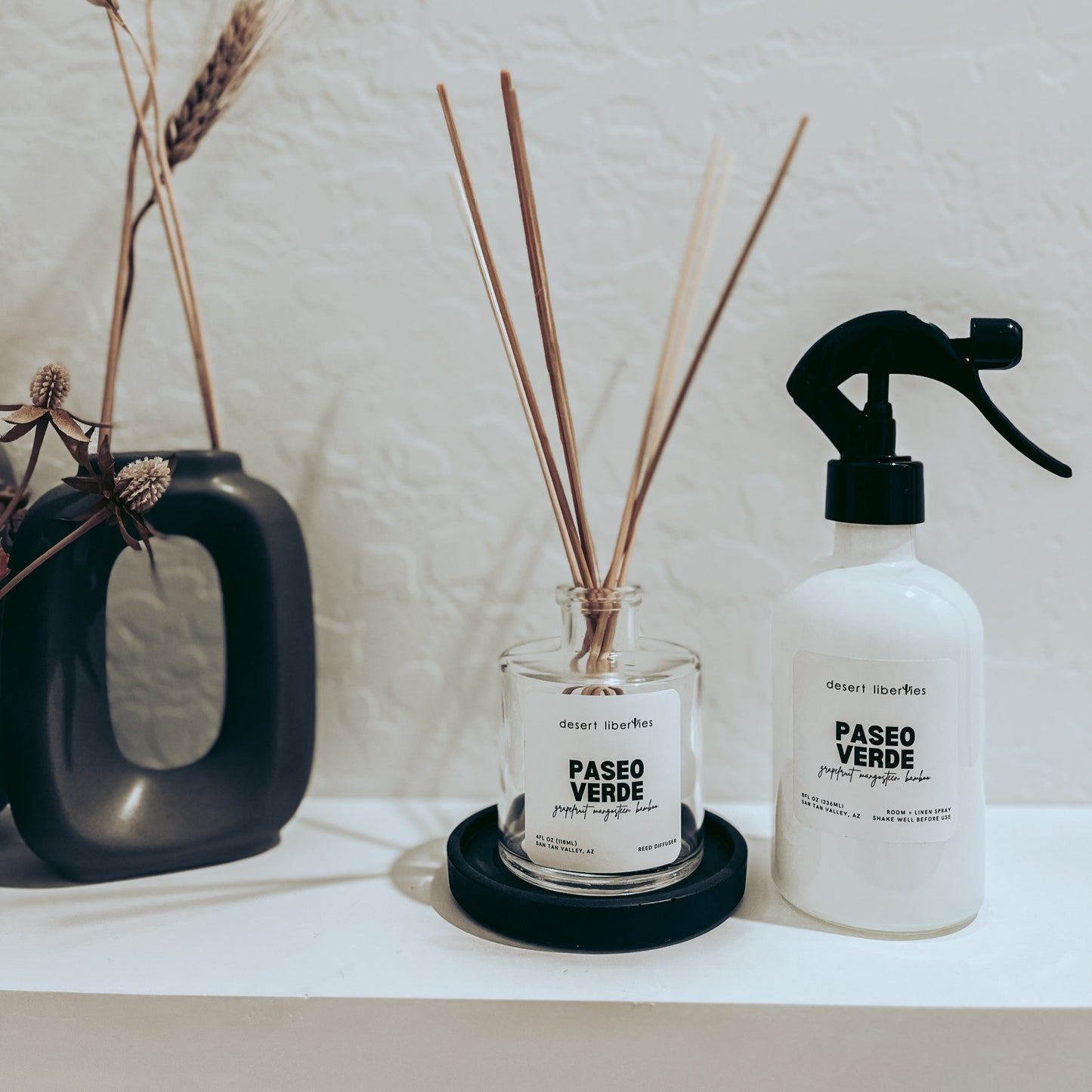 Decorative items including a diffuser, and spray bottle on a shelf with a neutral background.