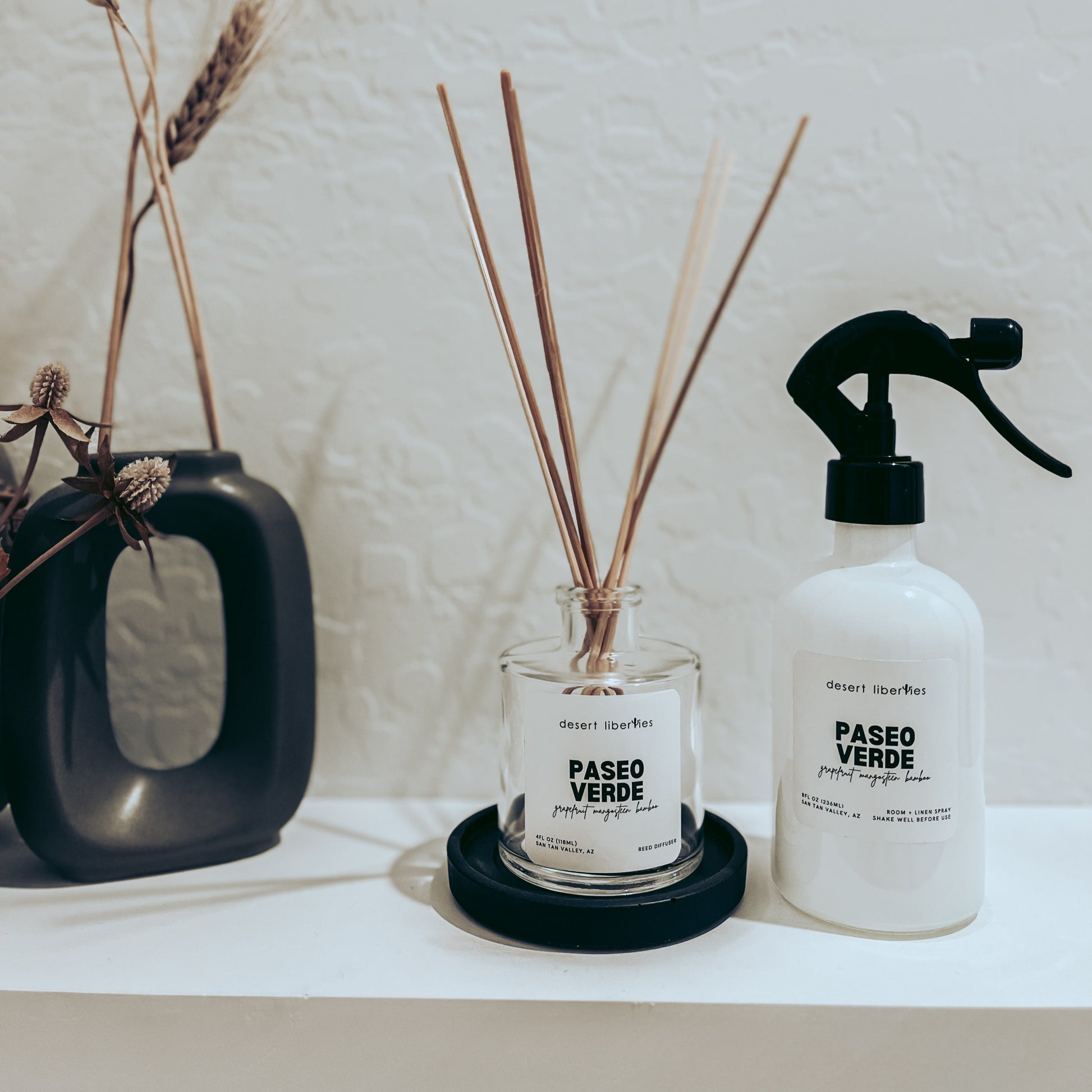 Decorative items including a diffuser, and spray bottle on a shelf with a neutral background.