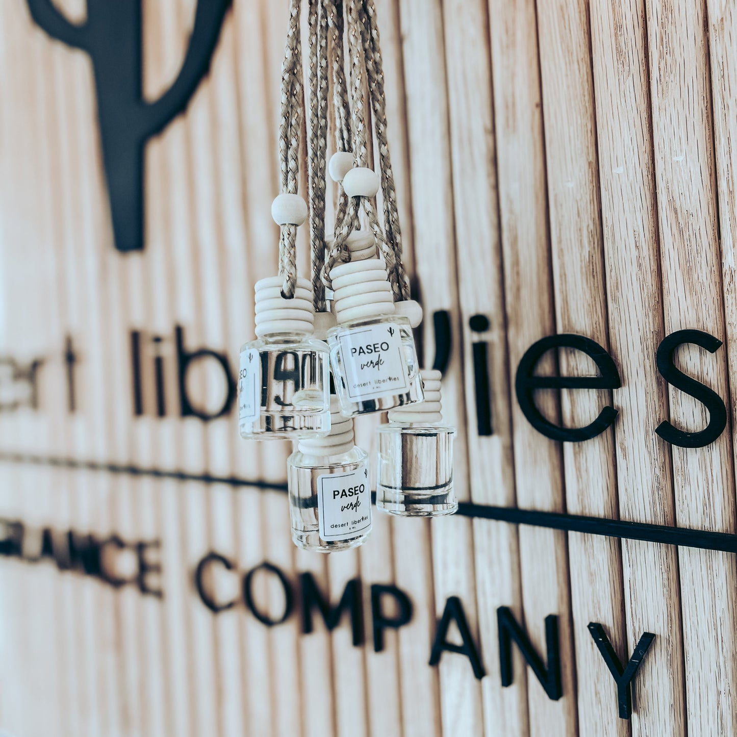 Hand holding multiple small diffuser bottles with visible brand names against a wooden background.
