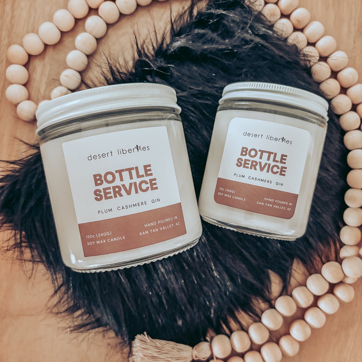Two candles labeled 'Bottle Service' on a wooden surface with decorative beads and fur.