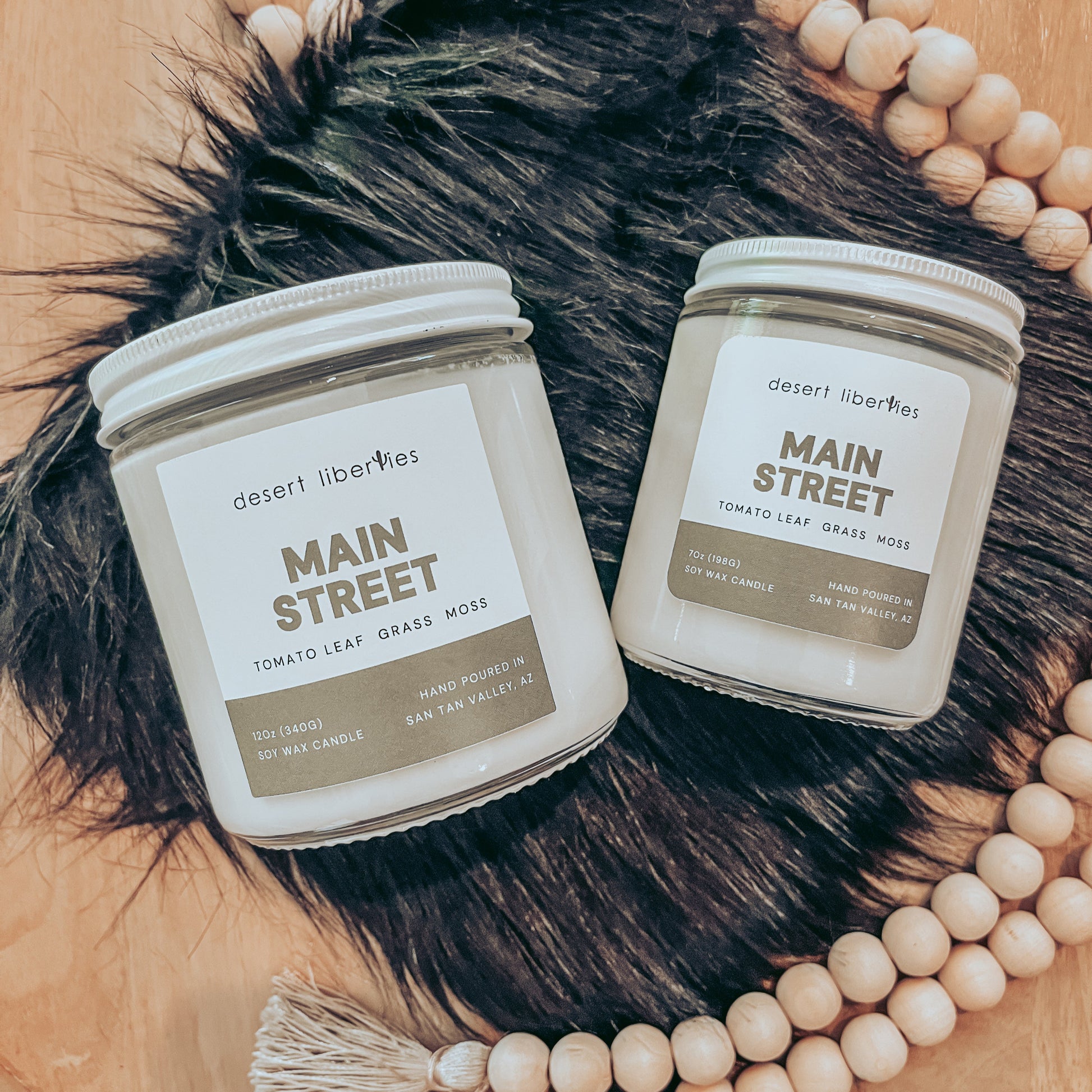 Two candles labeled 'Main Street' on a fur surface with beads around