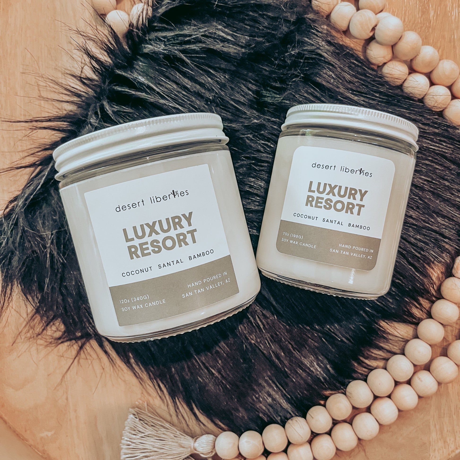 Two 'Luxury Resort' candles on a wooden surface with beads and fur.