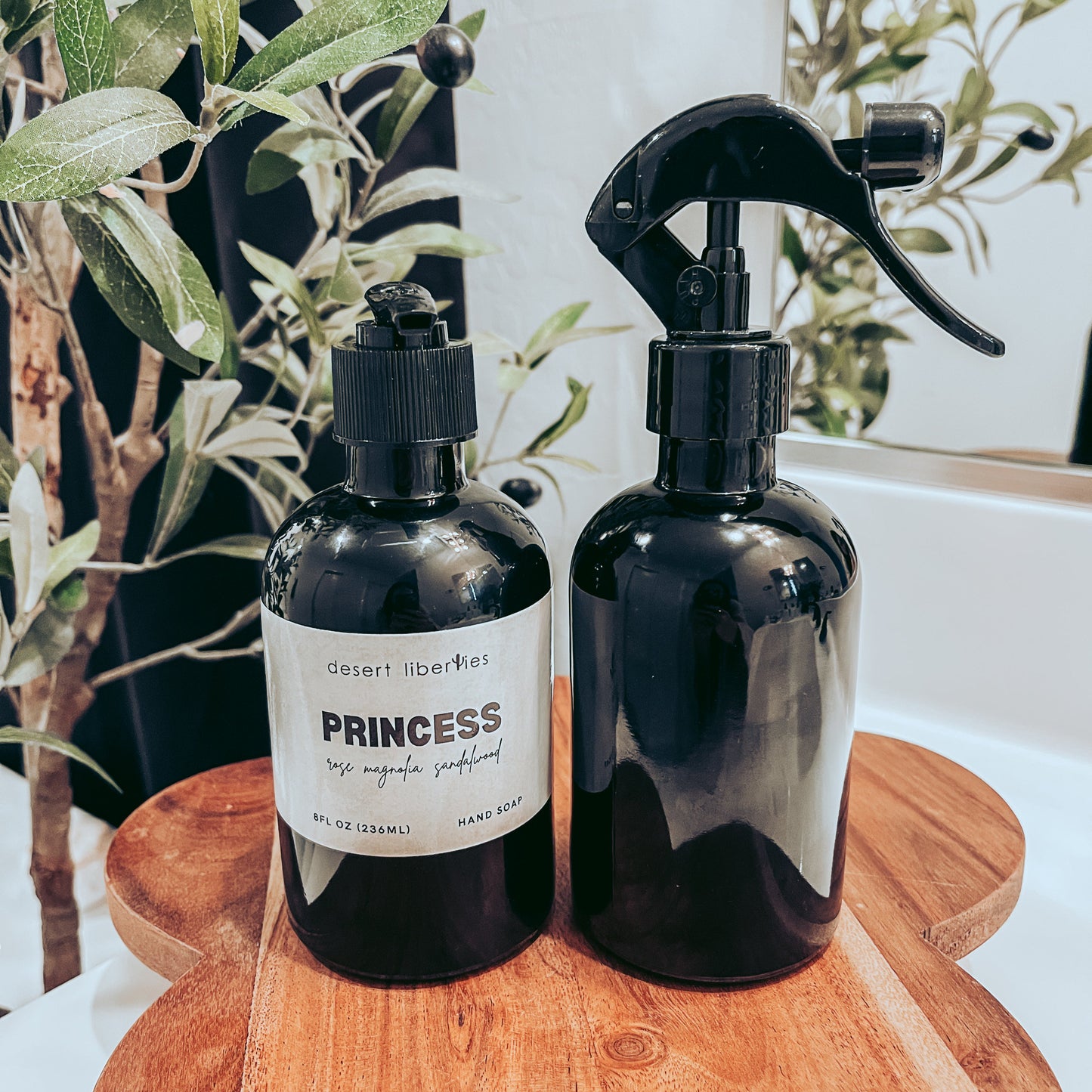 Soap bottle next to an unlabeled spray bottle on a wood surface and olive tree in the background. 