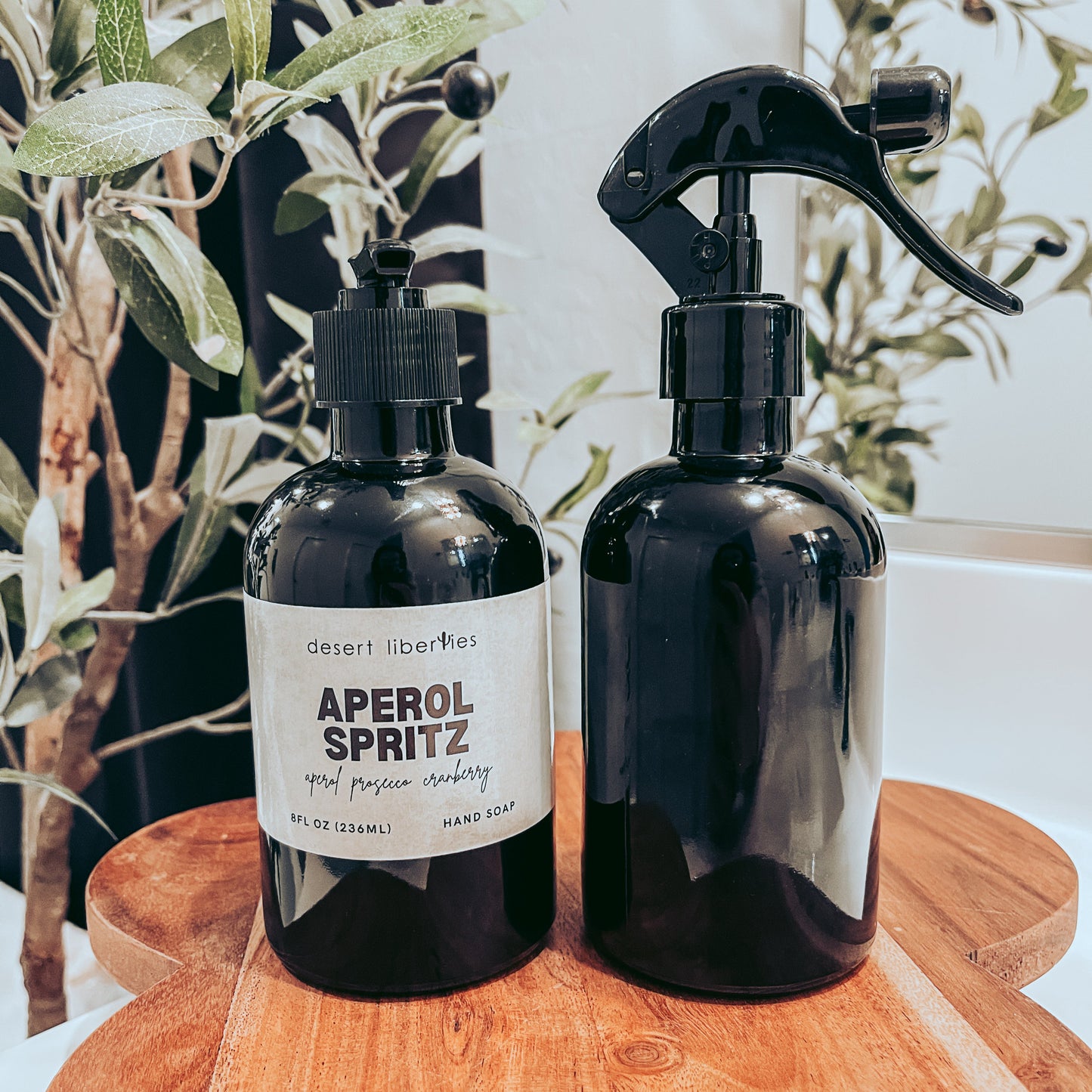 Soap bottle next to an unlabeled spray bottle on a wood surface and olive tree in the background. 