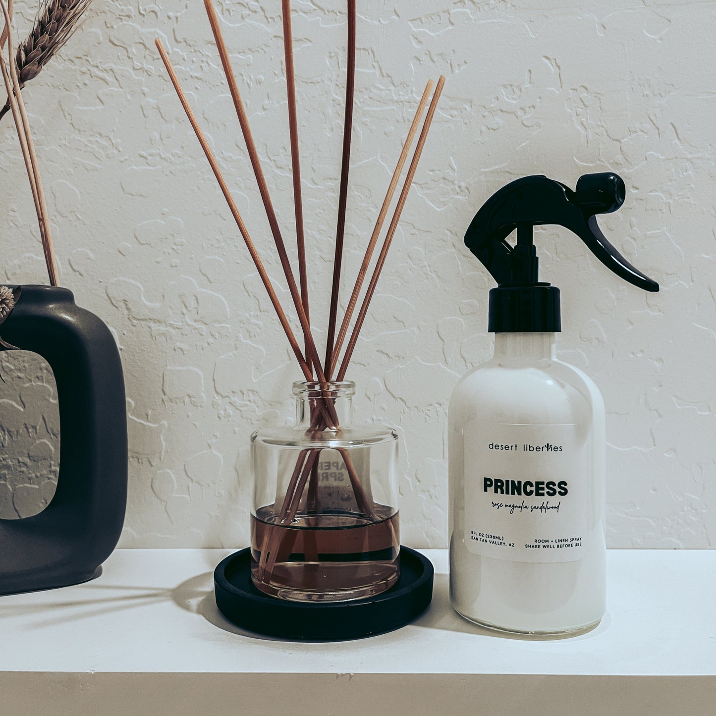 Diffuser with reeds and a spray bottle labeled 'Princess' on a white surface.