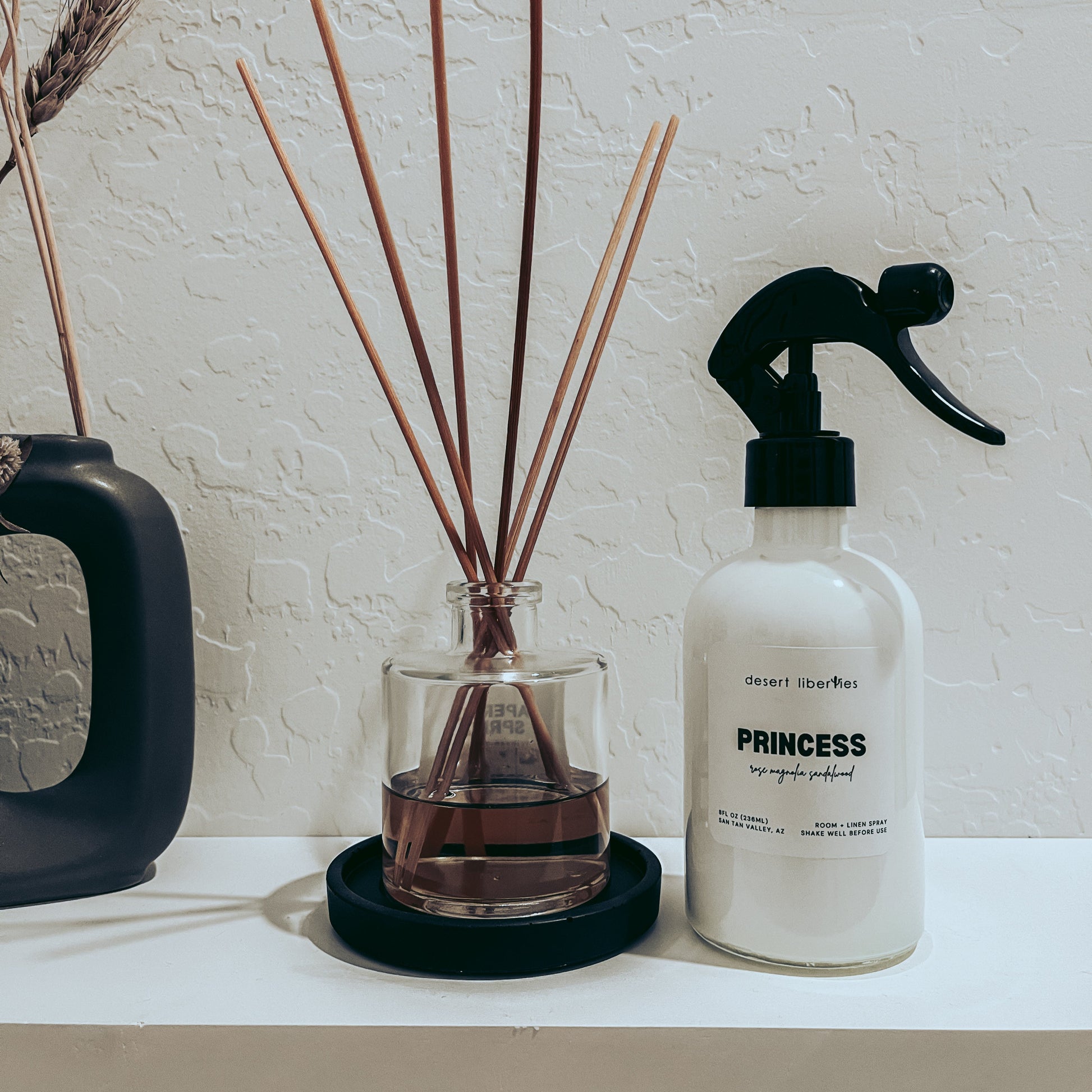 Diffuser with reeds and a spray bottle labeled 'Princess' on a white surface.