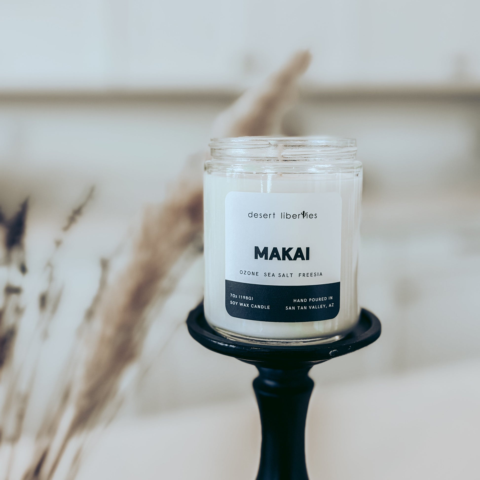 Candle labeled 'Makai' on a black holder with a blurred natural background