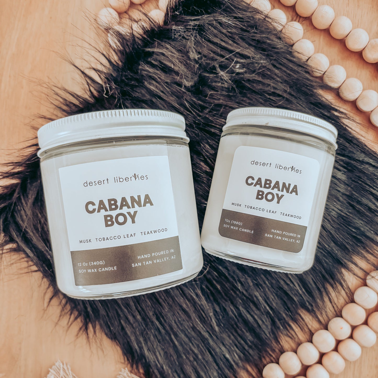 Two 'Cabana Boy' candles on a fur surface with beads in the background