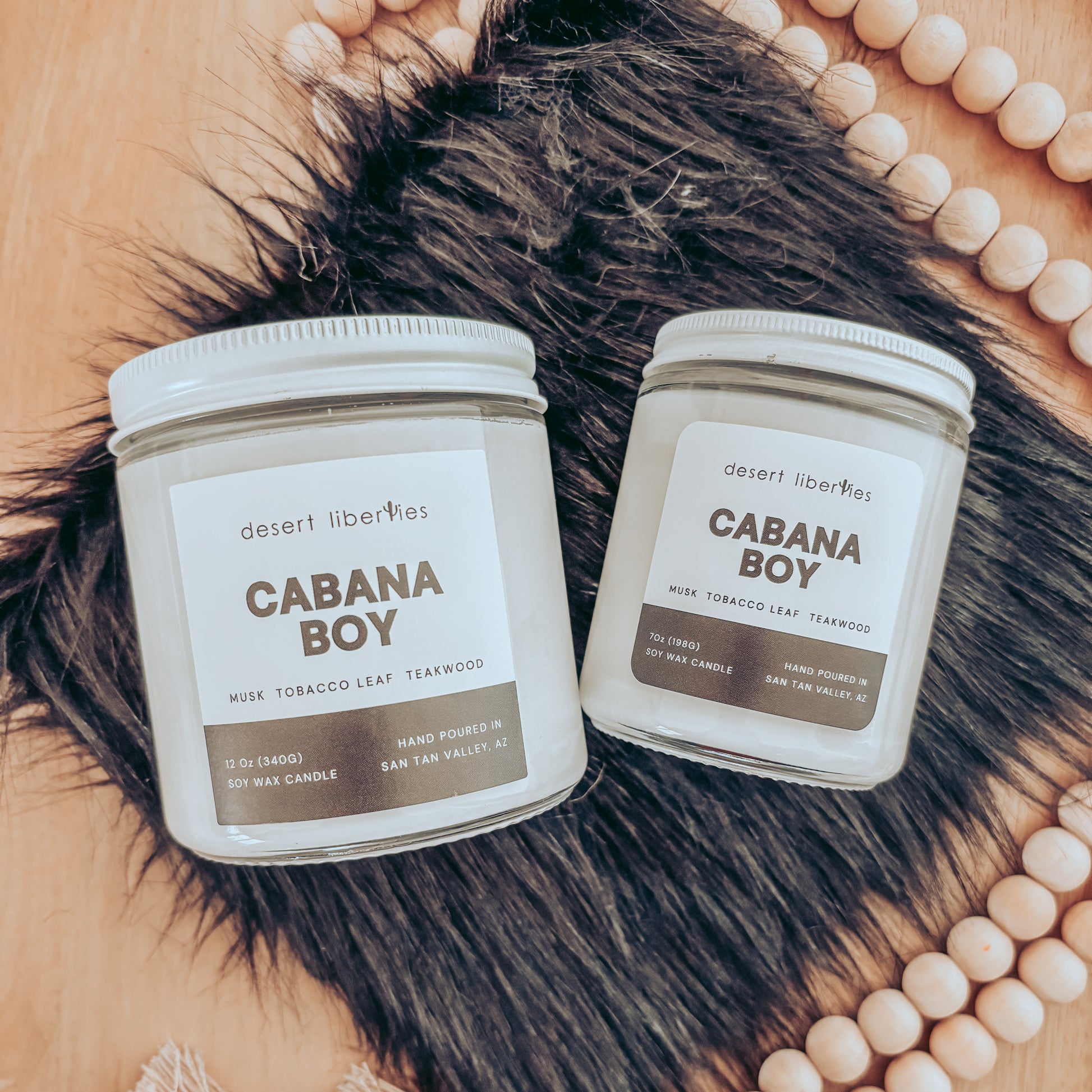 Two 'Cabana Boy' candles on a fur surface with beads in the background