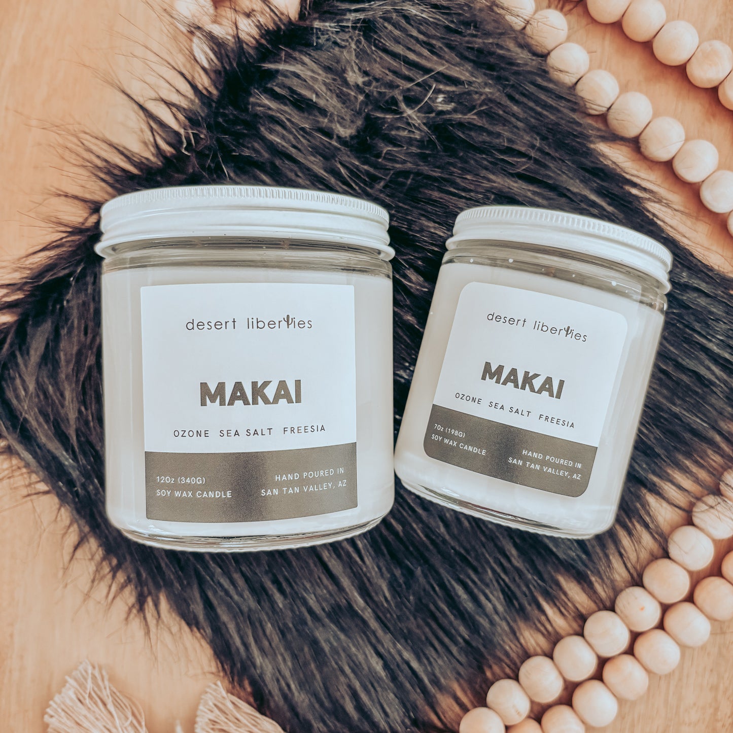 Two Makai candles from Desert Liberties on a wooden surface with decorative beads.