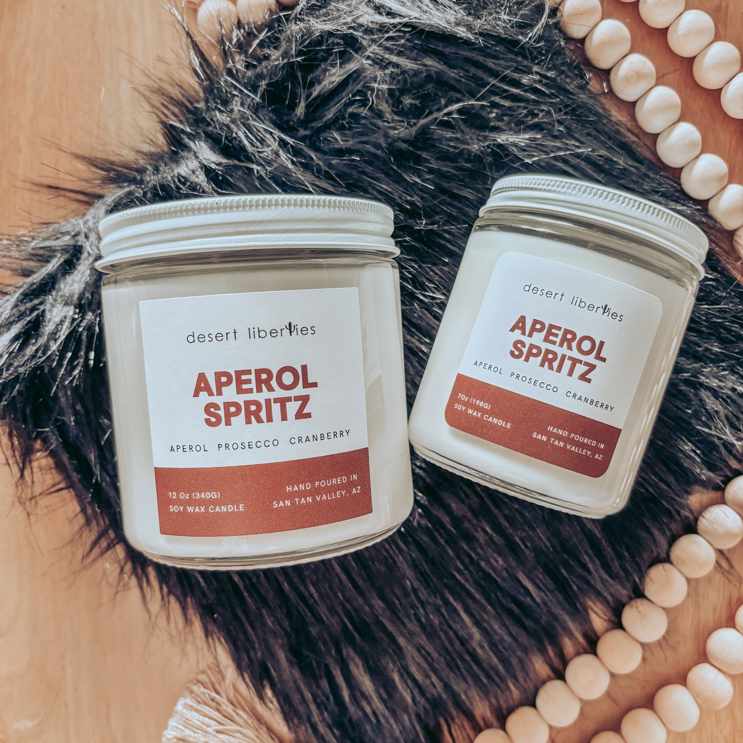 Two Aperol Spritz candles on a fur surface with decorative beads in the background