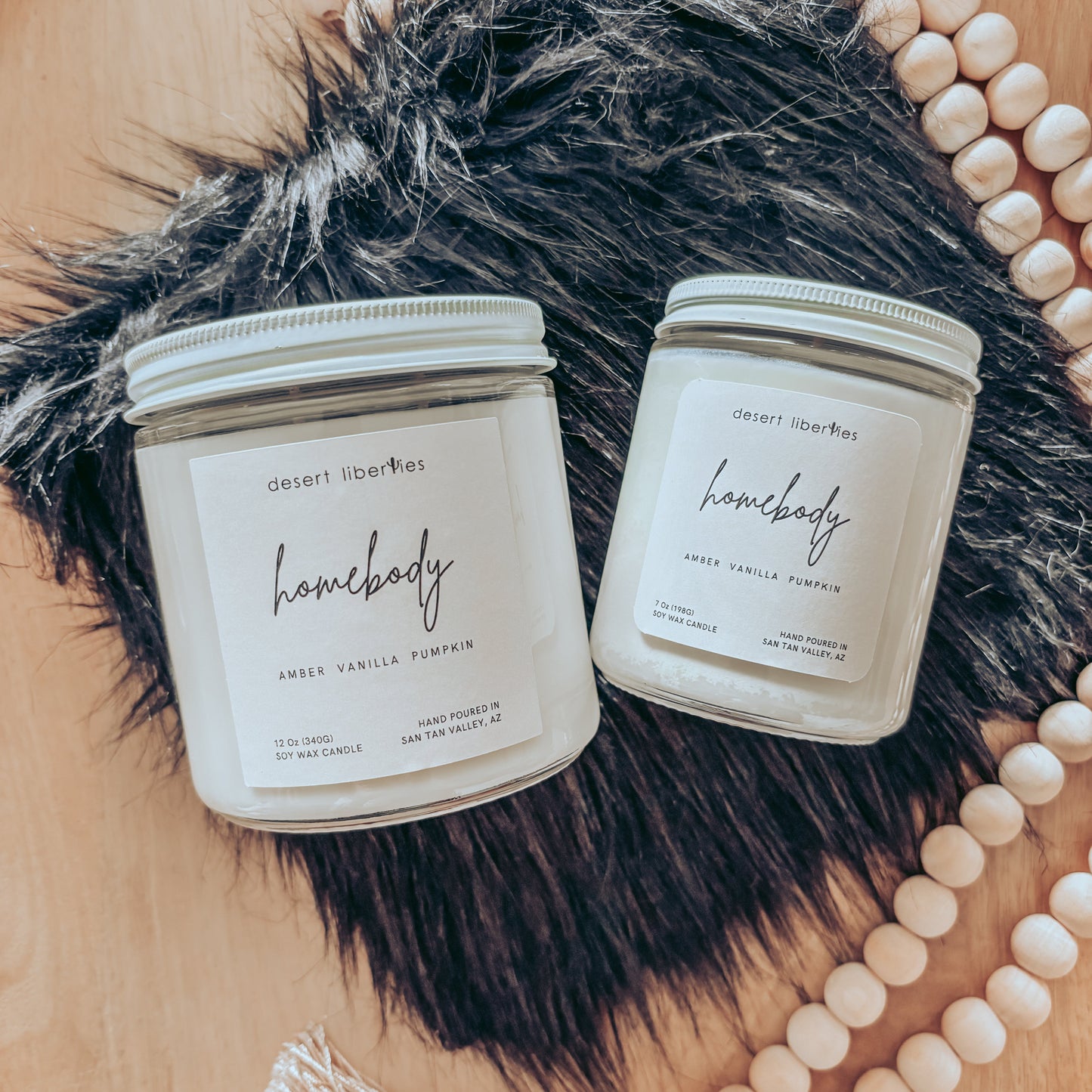 Two 'Homebody' candles on a fur surface with decorative beads in the background