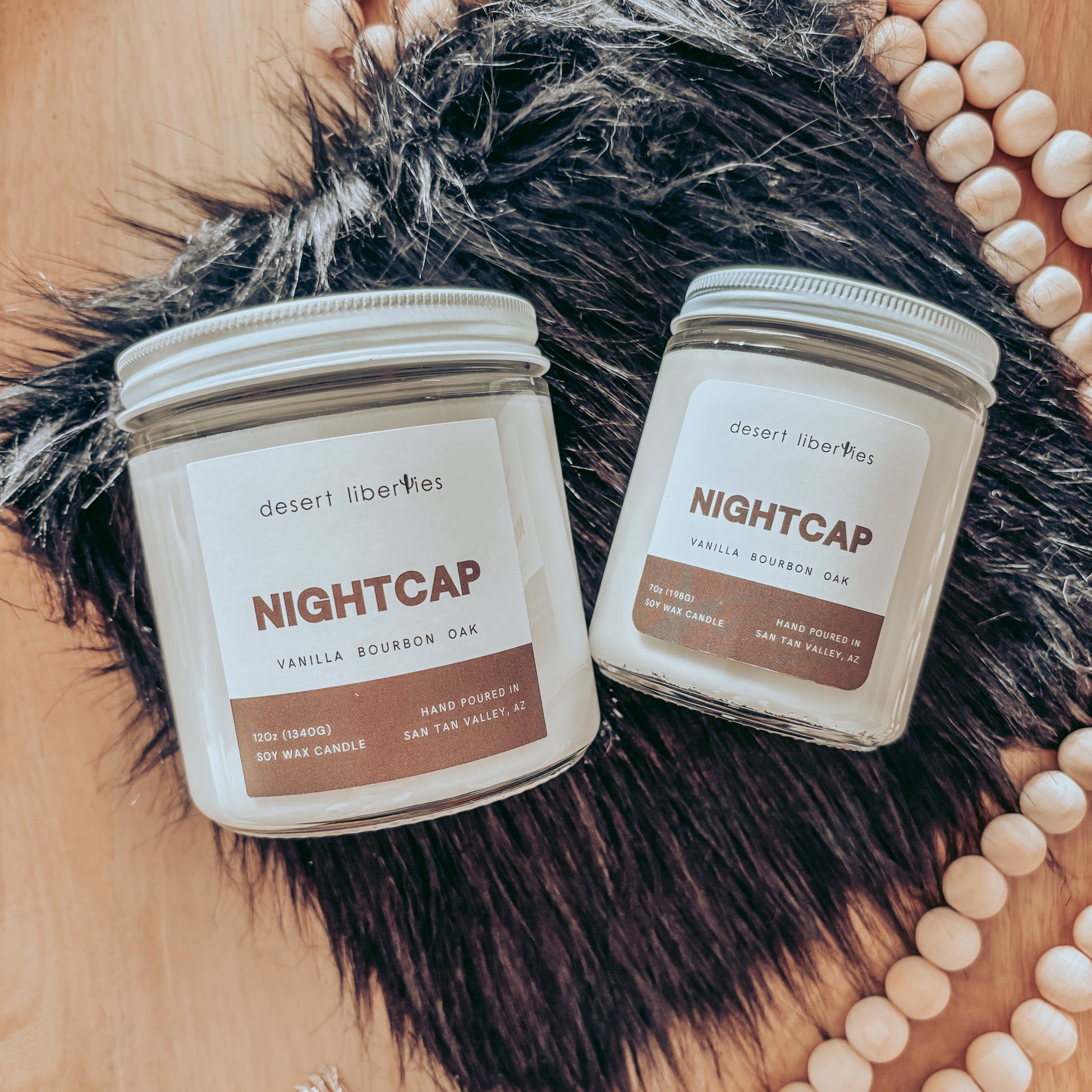 Two 'Nightcap' candles from Desert Liberties on a fur surface with decorative beads.