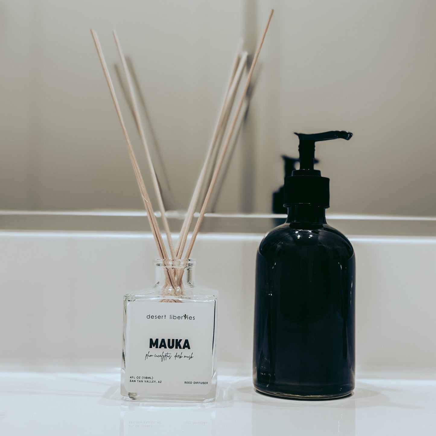 Reed diffuser and black bottle on a white surface with neutral background