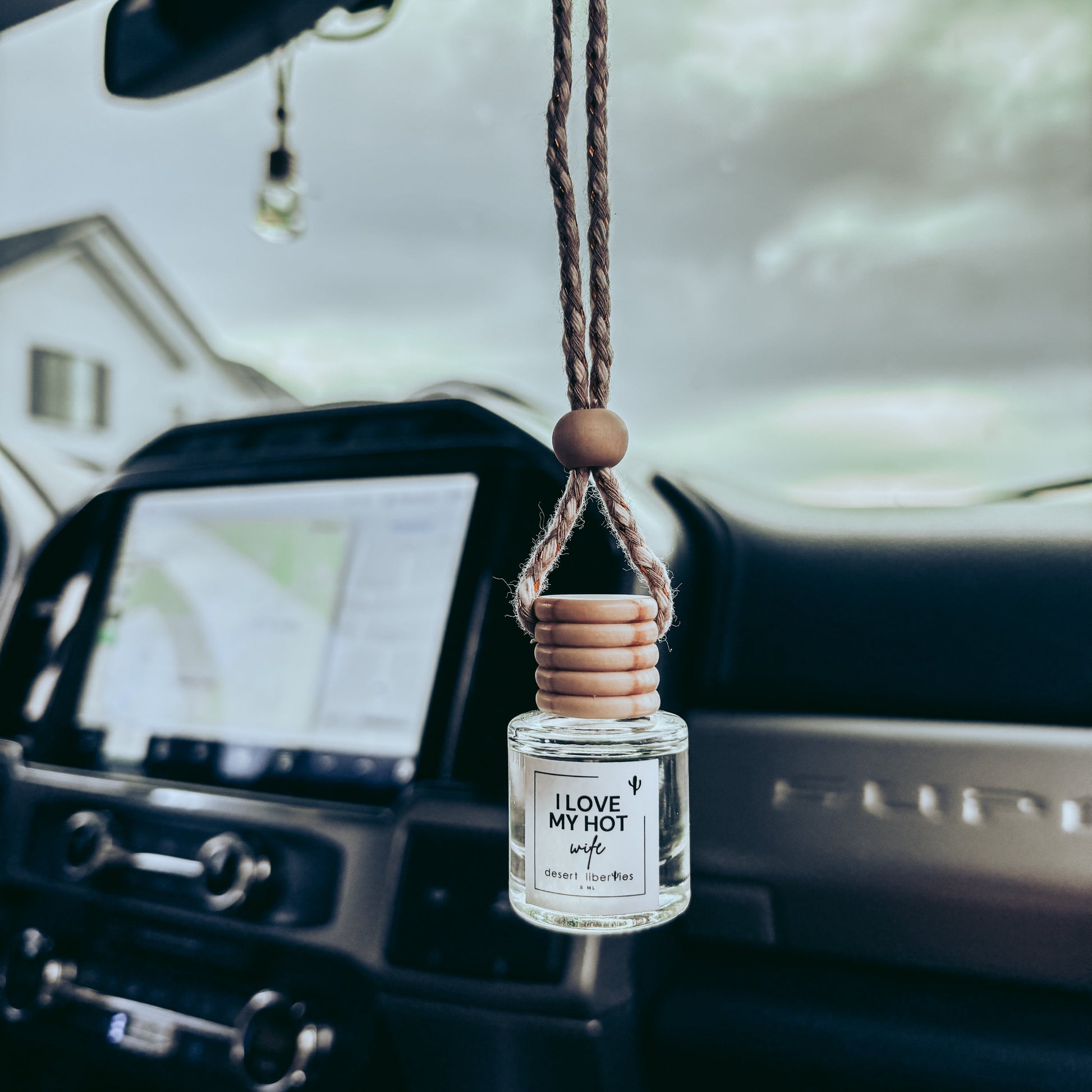 Car air freshener hanging from a car's rearview mirror with a scenic background.