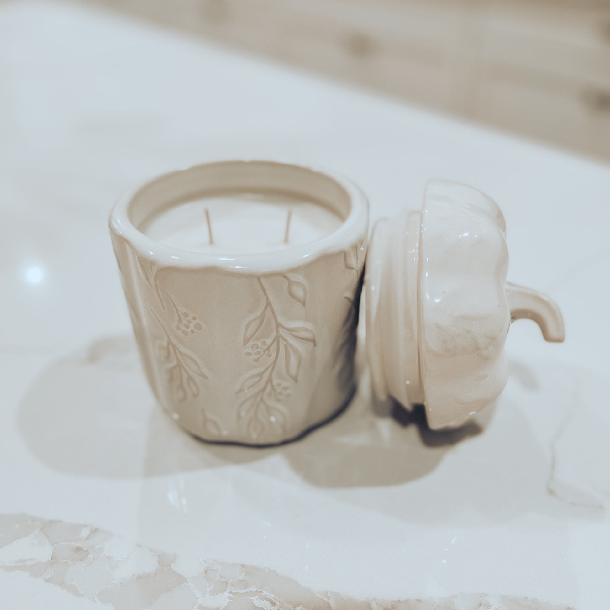 Ivory pumpkin canister candle, with top off, on a white marble surface. 