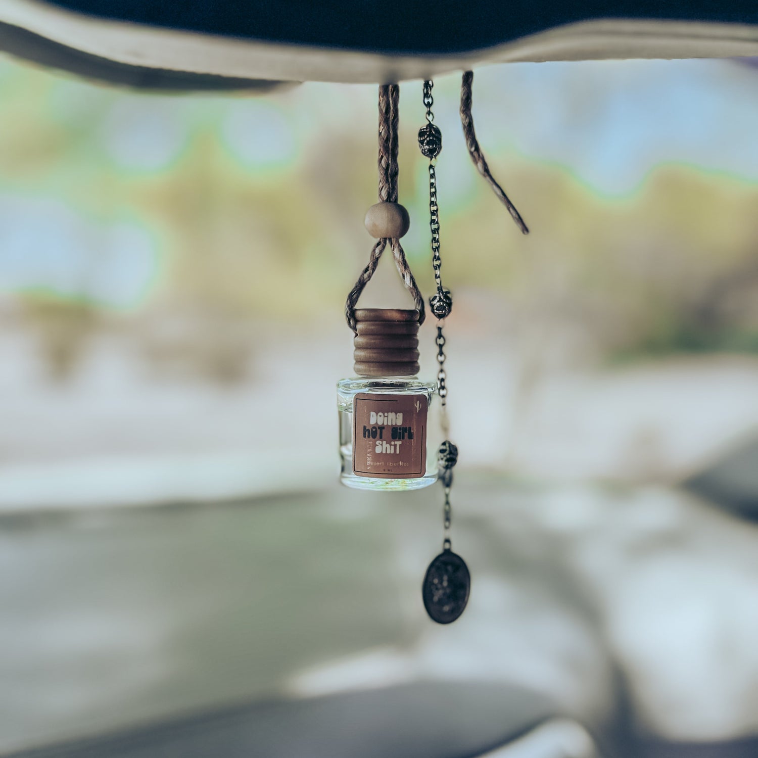 Car hanging ornament with a small bottle inside, hanging from a car's rearview mirror.