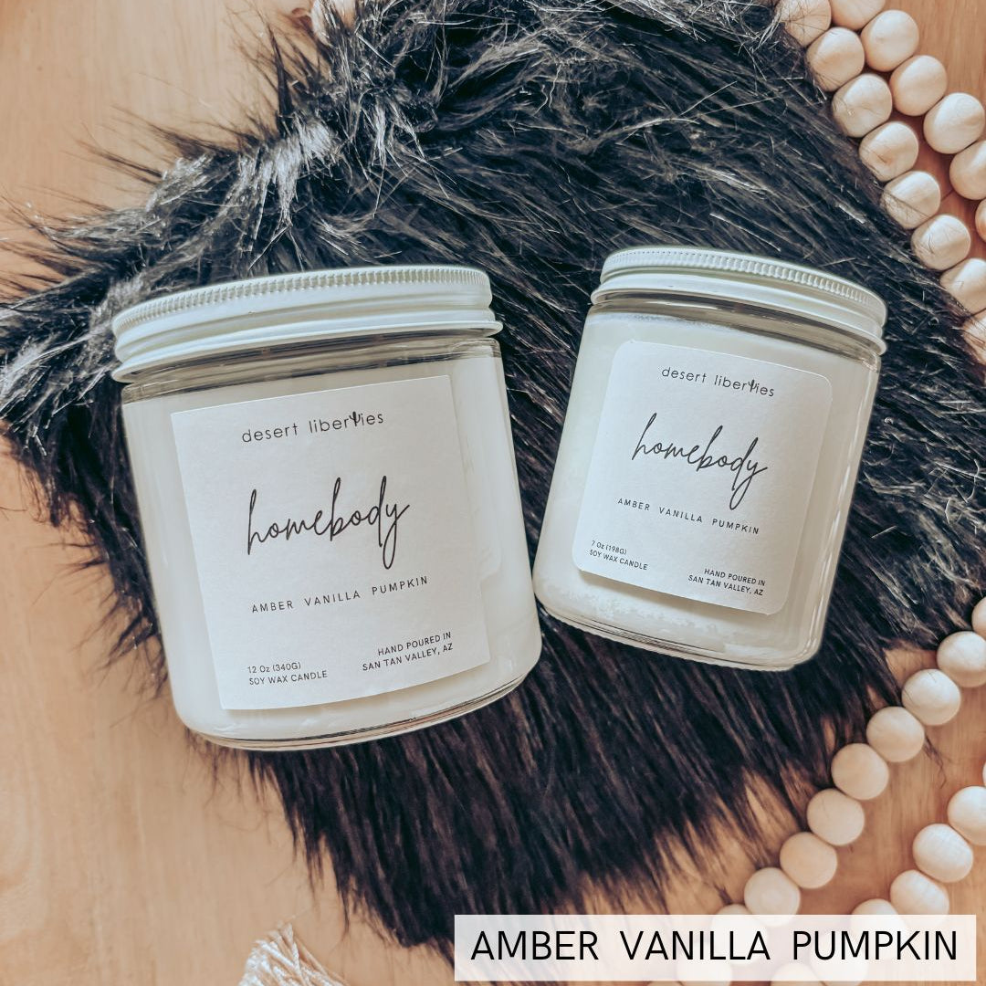 Two 'homebody' candles on a fur surface with decorative beads and text overlay.