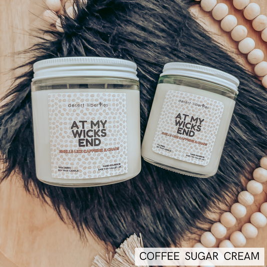 Two candles labeled 'At My Wicks End' on a textured surface with beads and fur.
